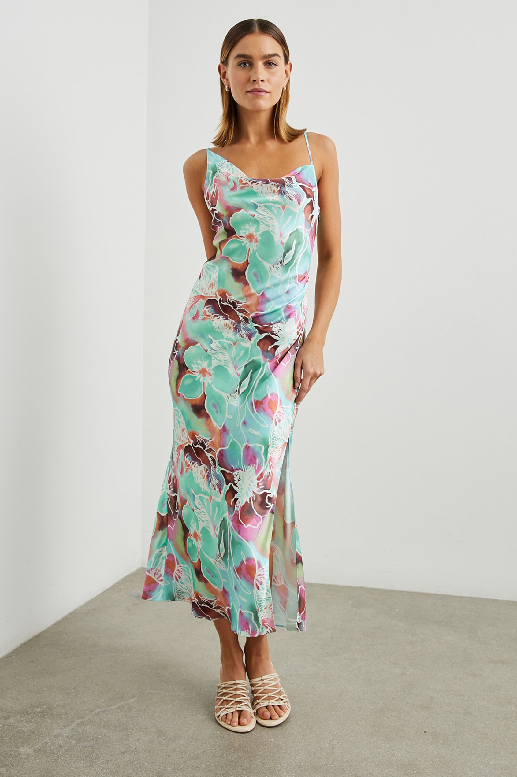 Lotus Sleeveless Midi Dress with an Asymmetrical Cowl Neck, Adjustable Back Spaghetti Straps, a Side Slit, Light Ruching on one Bodice Side in Kauai Floral Colorway, in Greens, Browns, Pinks, and White - Front Full Body View Featured on Model