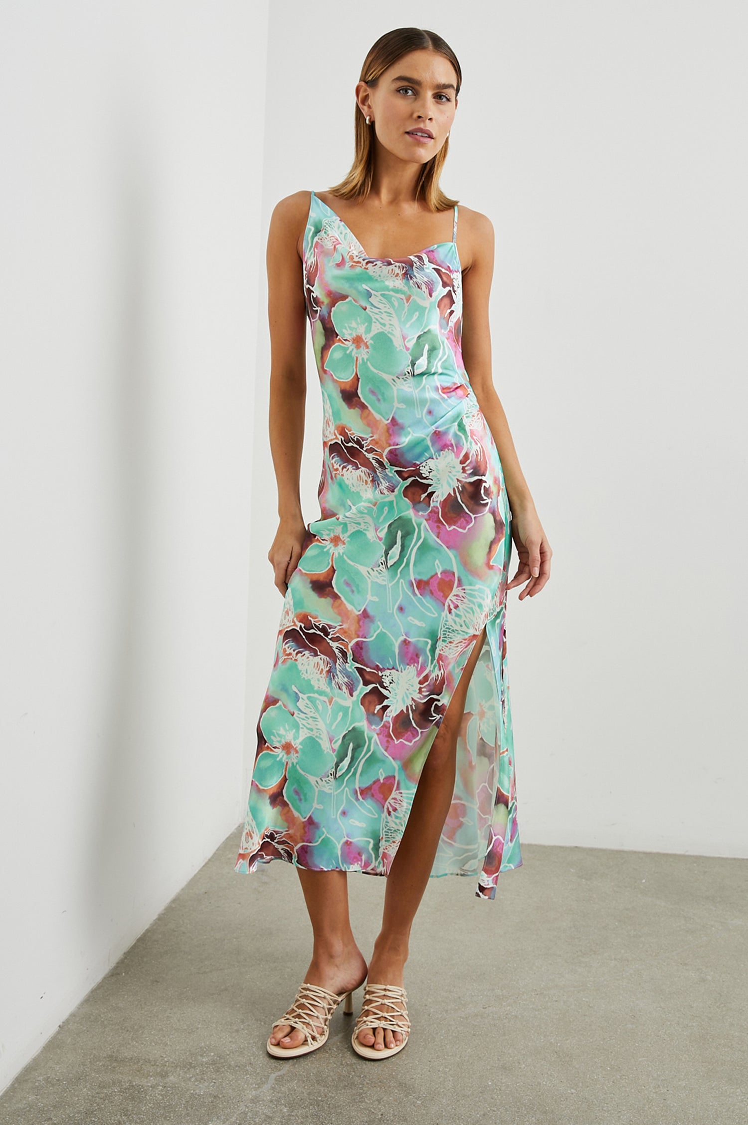 Lotus Sleeveless Midi Dress with an Asymmetrical Cowl Neck, Adjustable Back Spaghetti Straps, a Side Slit, Light Ruching on one Bodice Side in Kauai Floral Colorway, in Greens, Browns, Pinks, and White - Front Full Body View Featured on Model