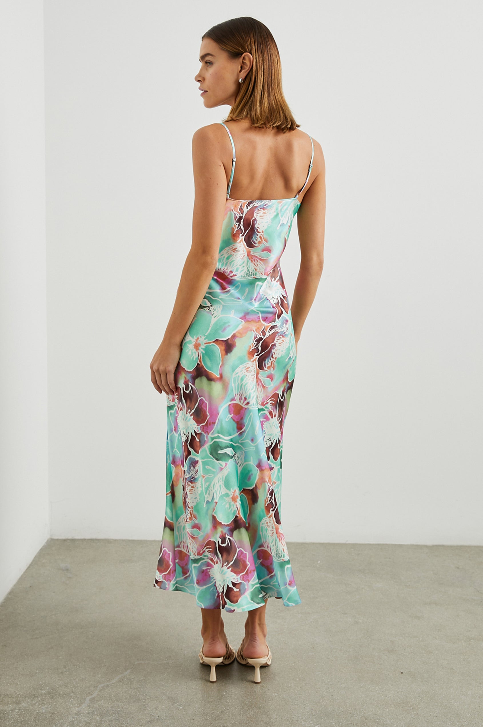 Lotus Sleeveless Midi Dress with an Asymmetrical Cowl Neck, Adjustable Back Spaghetti Straps, a Side Slit, Light Ruching on one Bodice Side in Kauai Floral Colorway, in Greens, Browns, Pinks, and White - Back Full Body View Featured on Model