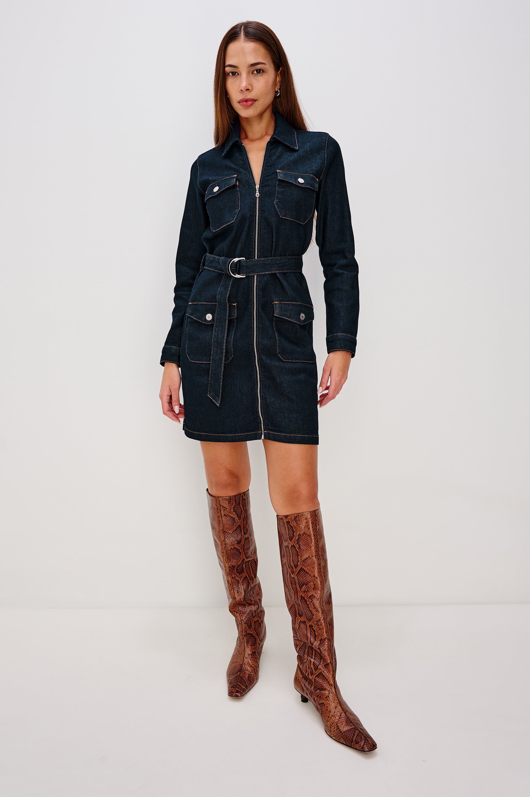 Jefferson is a long sleeve mini denim dress, featuring utility-inspired details and an o-ring adjustable waist belt in Midnight Blue colorway, a rinse wash. Front full body view featured on model.