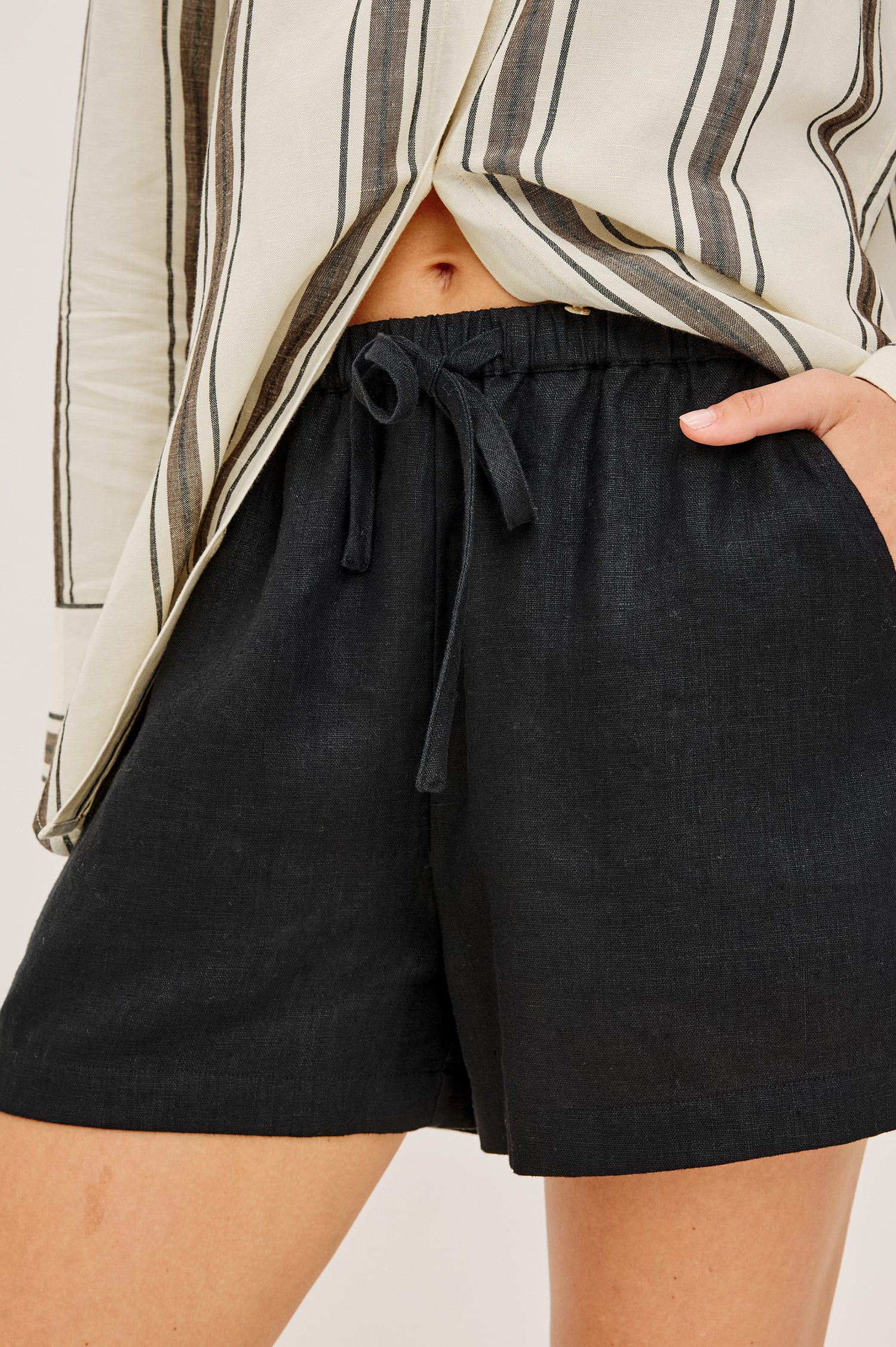 Jenner Short in Linen With High-Rise, Adjustable Drawstring Ties, Relaxed Fit, and Side Pockets in Black Colorway - Lower Body Front View Featured on Model