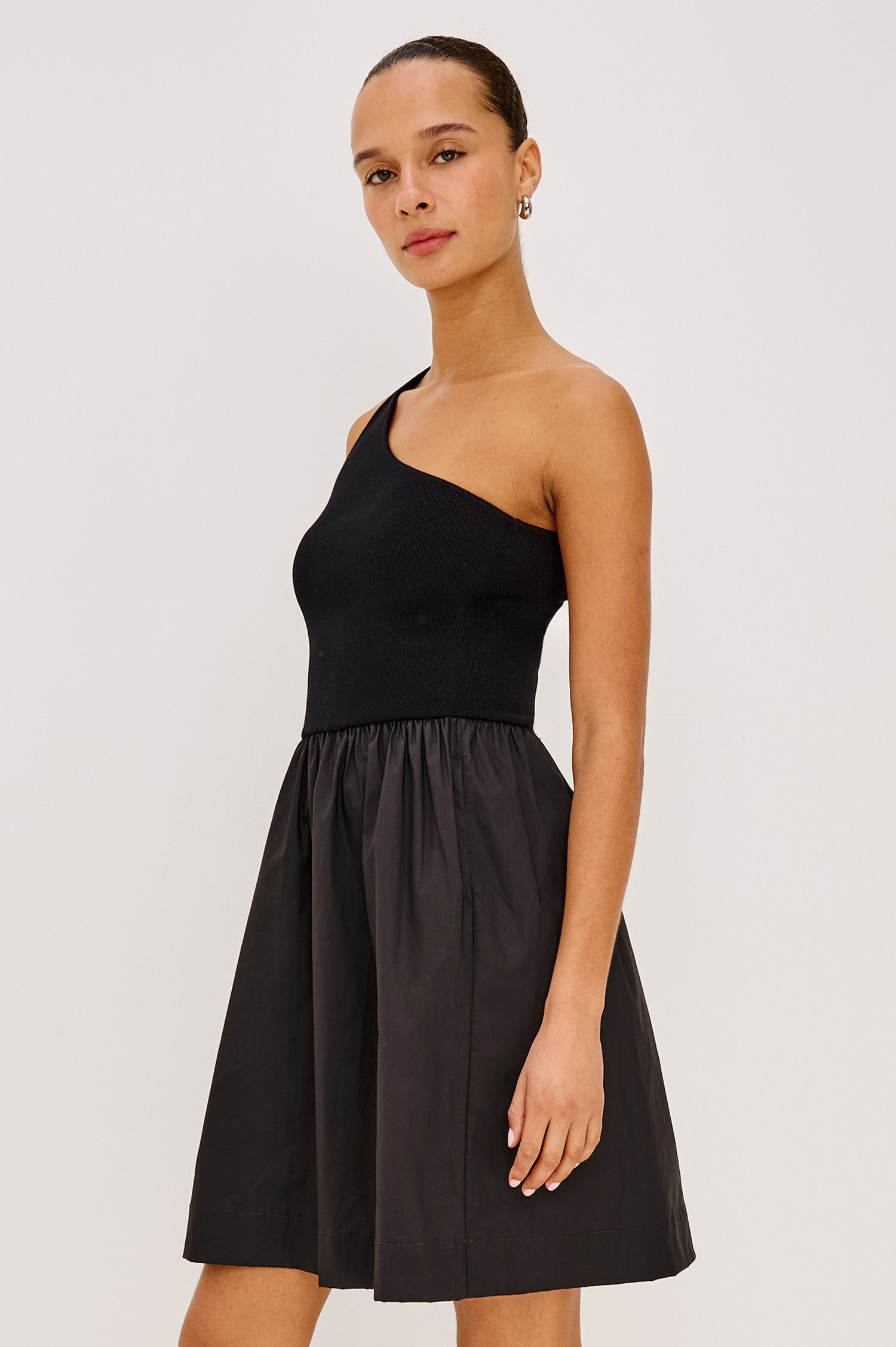 Joanne Mini Dress With One-Shoulder Neckline, Soft Jersey Bodice, Dropwaist Cotton Poplin Skirt, and Side Pockets in Black Colorway - Side Crop View On Model.