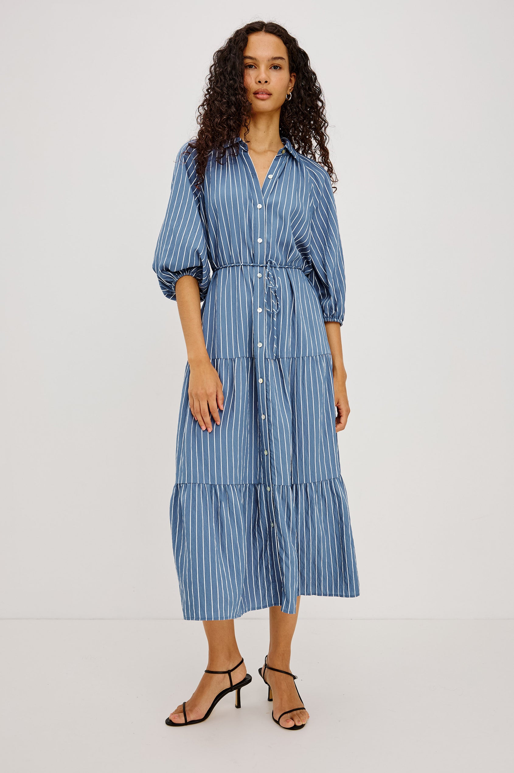 June Maxi Dress in Soft Crinkle Shirting With Three-Quarter Puff Sleeves, Point Collar, Full Front Button Placket, and Self-Tie Waist in Washed Indigo Stripe Colorway - Full Body Front View Featured on Model