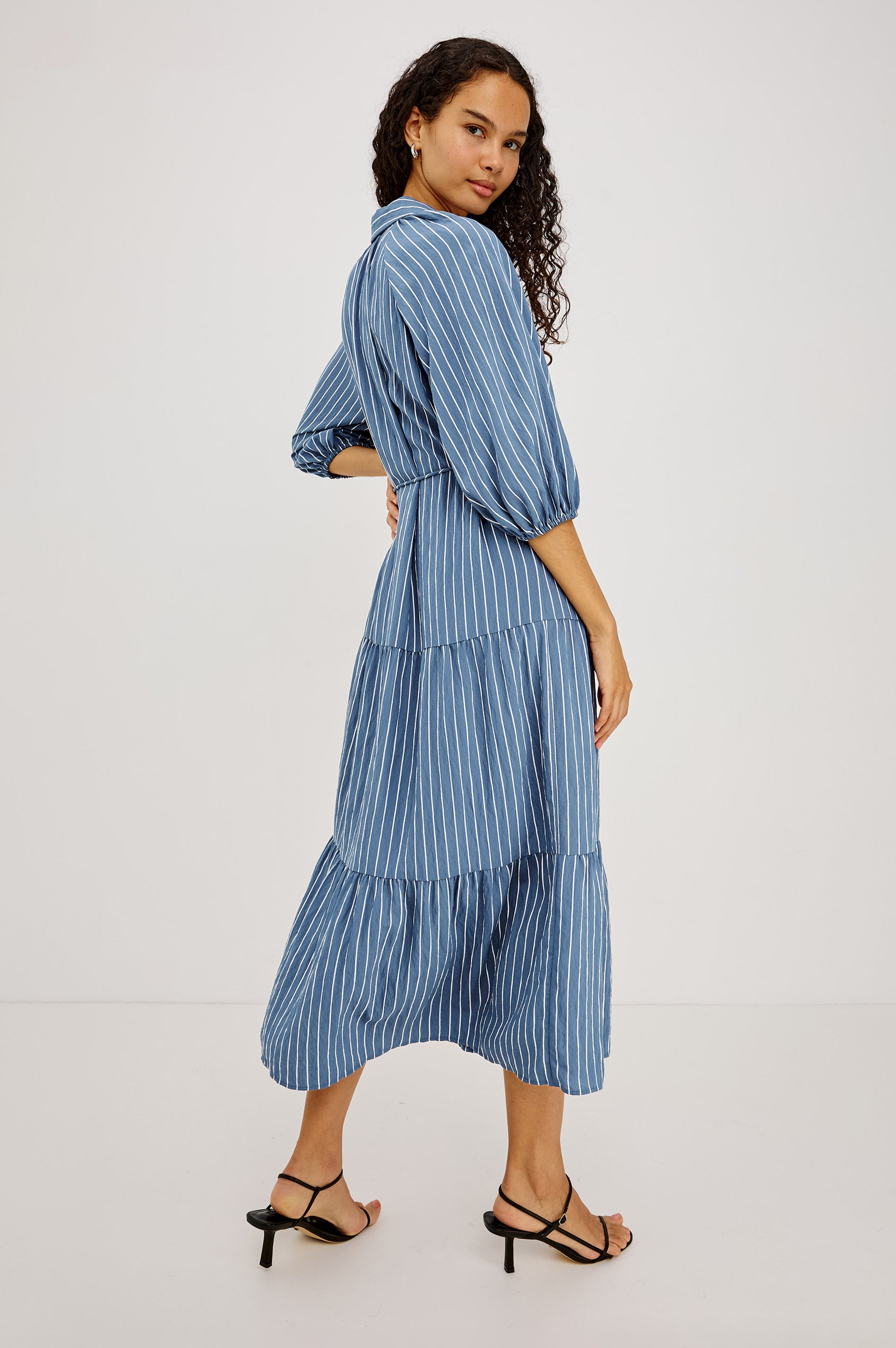 June Maxi Dress in Soft Crinkle Shirting With Three-Quarter Puff Sleeves, Point Collar, Full Front Button Placket, and Self-Tie Waist in Washed Indigo Stripe Colorway - Lower Body Back View Featured on Model