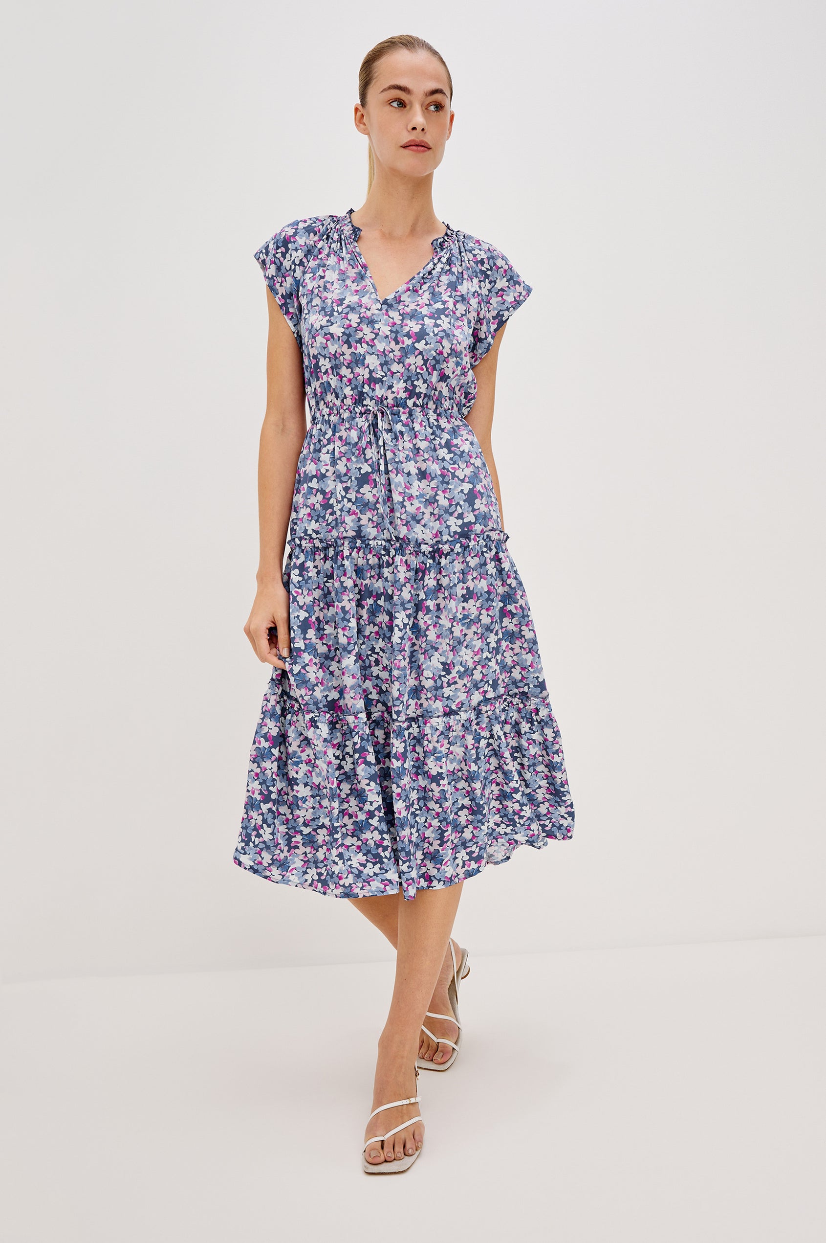Juni Tiered Midi Dress with a V-Neck, Ruffled Neckline, Short Flutter Sleeves, Drawstring Waist Detail in Blue Blossom Colorway. Full Body Front View Shown on Model. 