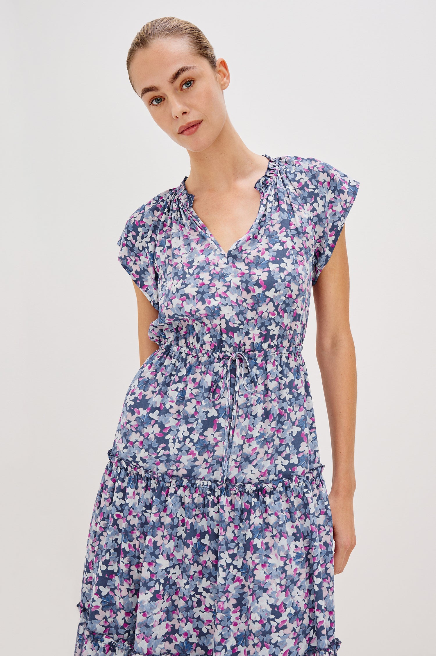 Juni Tiered Midi Dress with a V-Neck, Ruffled Neckline, Short Flutter Sleeves, Drawstring Waist Detail in Blue Blossom Colorway. Front View Shown on Model. 
