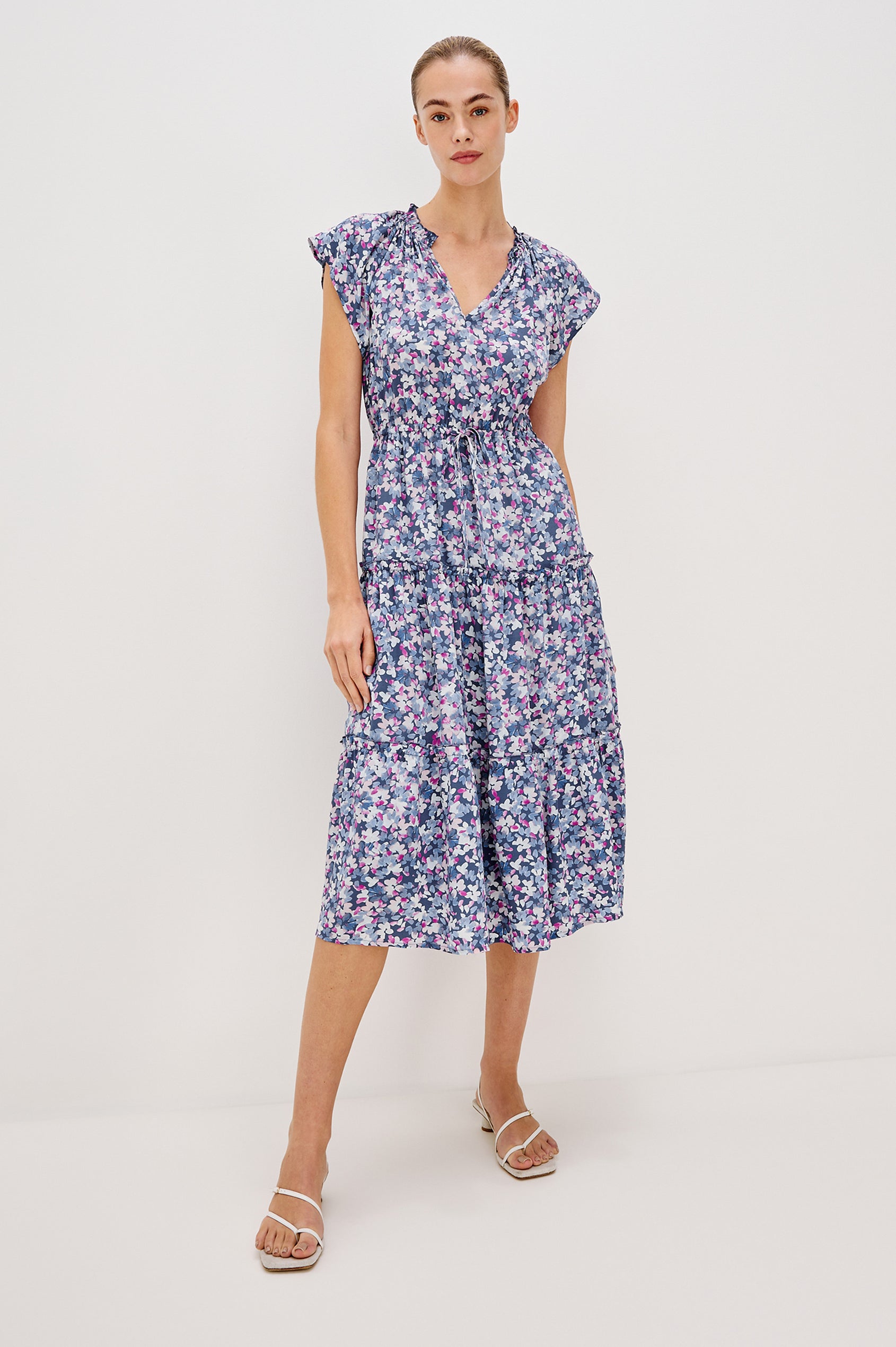Juni Tiered Midi Dress with a V-Neck, Ruffled Neckline, Short Flutter Sleeves, Drawstring Waist Detail in Blue Blossom Colorway. Full Body Front View Shown on Model. 