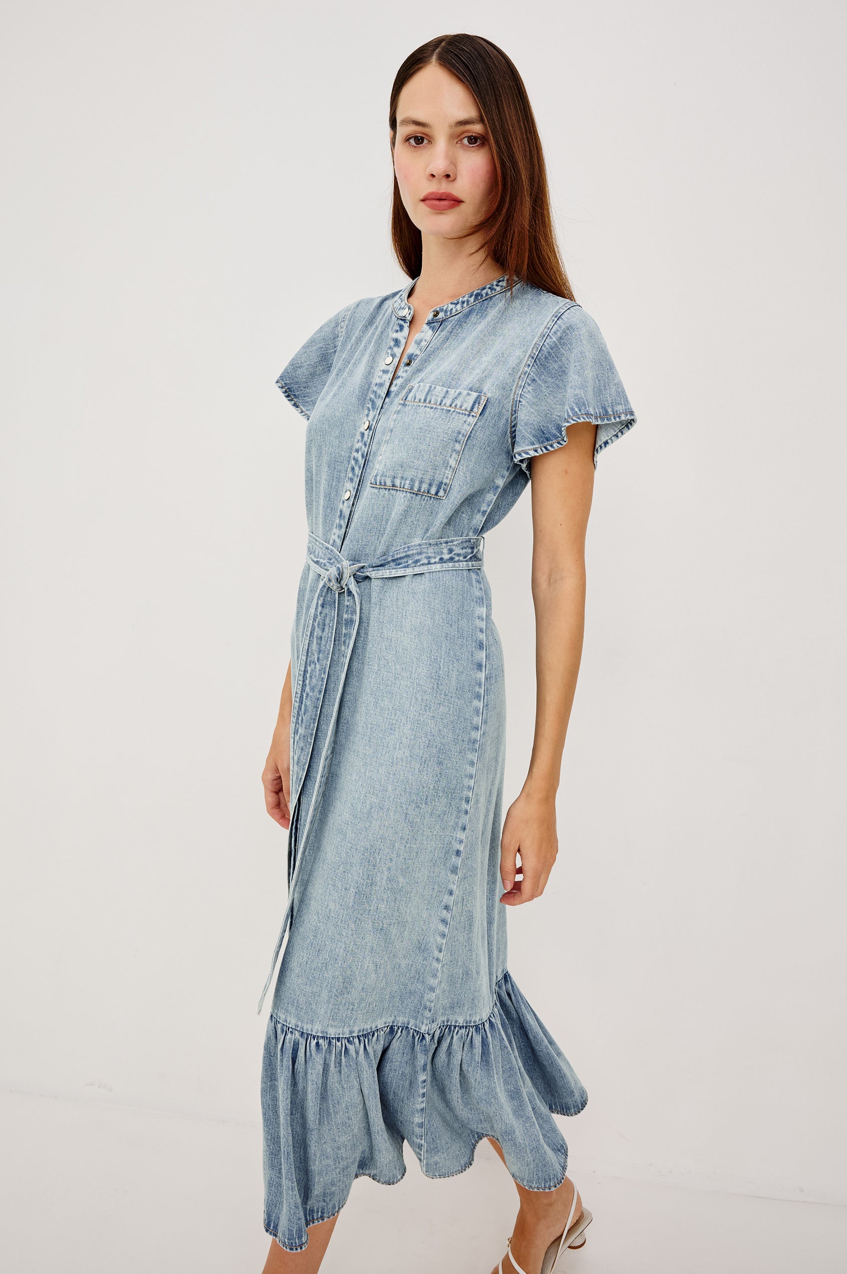 Kahlo TENCELâ„¢ Denim Shirt Dress With Short Flutter Sleeves Front Buttons a Single Chest Patch Pocket Adjustable Belted Ties Ruffle Hem in Faded Indigo Colorway - Full Body Front View Featured on Model