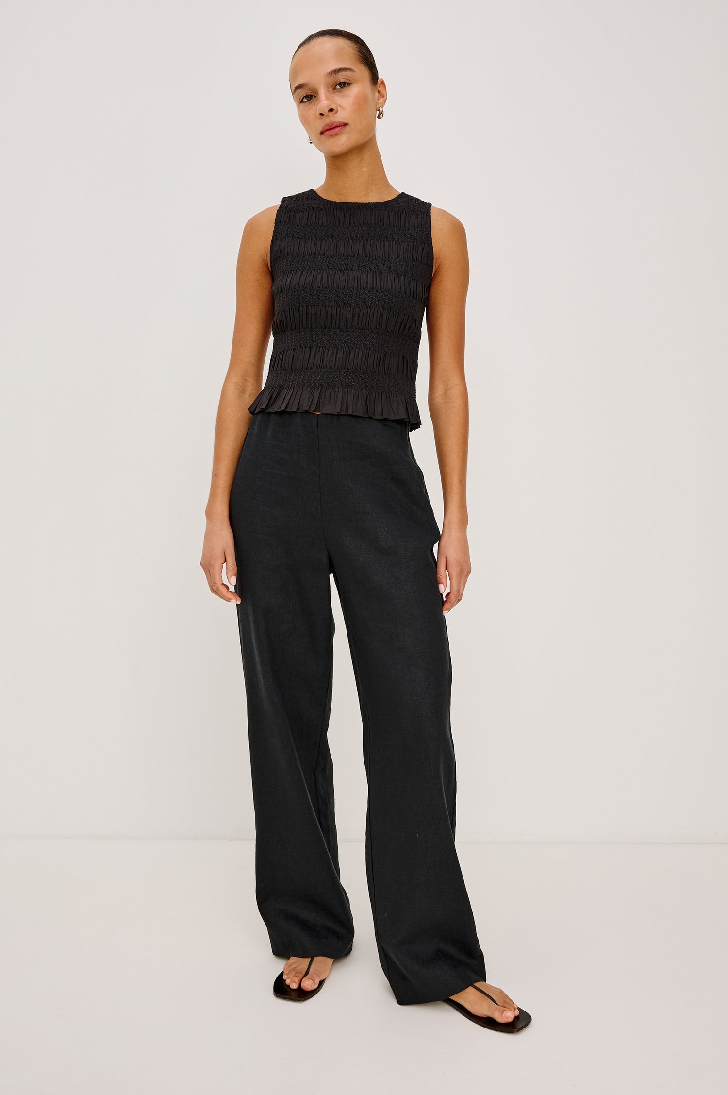 Kane Sleeveless Fitted Top in Cotton With Diamond Smocking All Over, High Boat Neckline, and Flared Ruffle Hem in Black Colorway - Full Body Front View Featured on Model