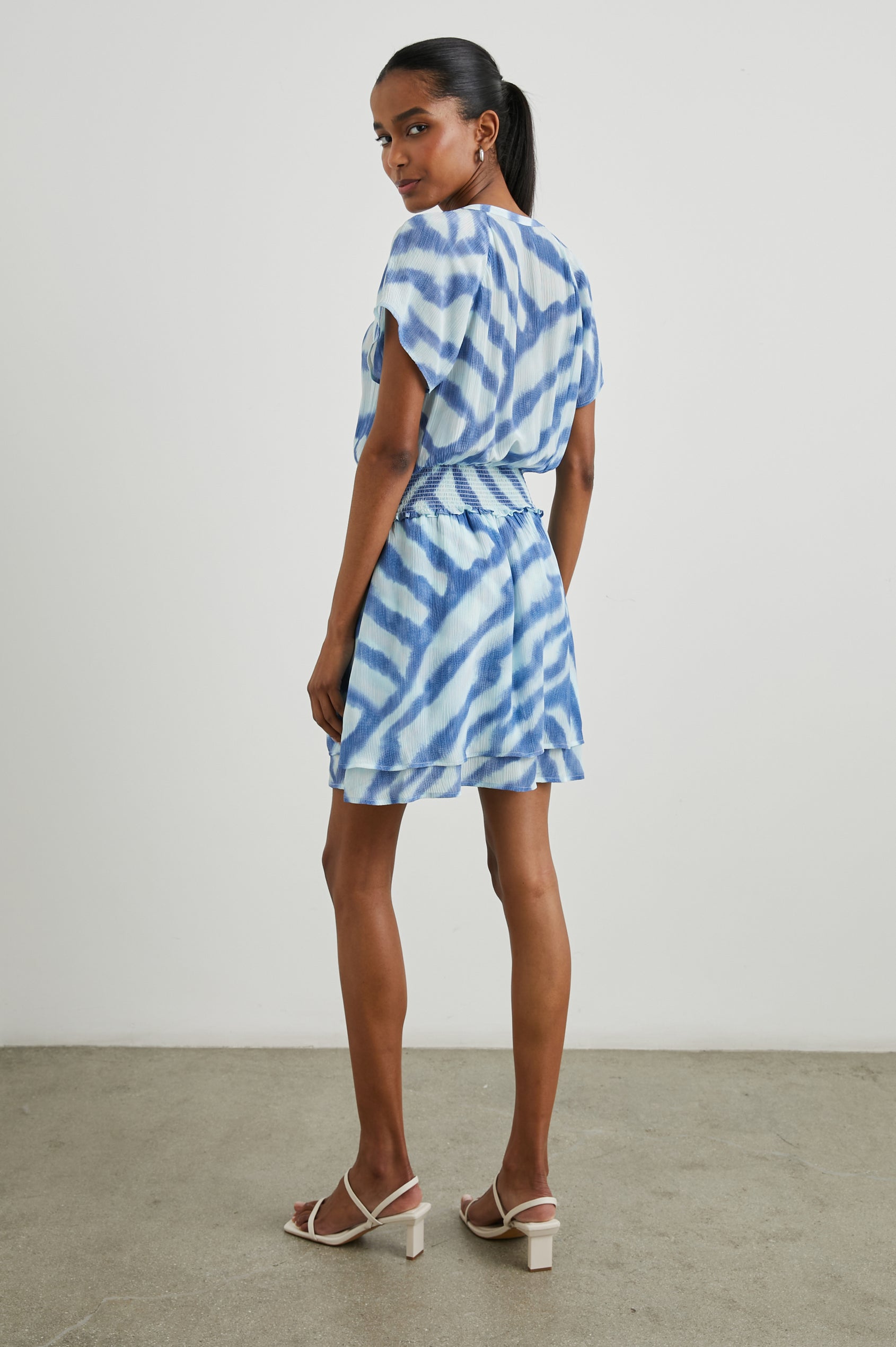 Karla Short Sleeve Mini Dress with a V Neck with Four Buttons, a Shirred Waist and a Double-Layered Skirt in Blue Watercolor Stripes Colorway, Blue on Light Blue - Back Full Body View Featured on Model