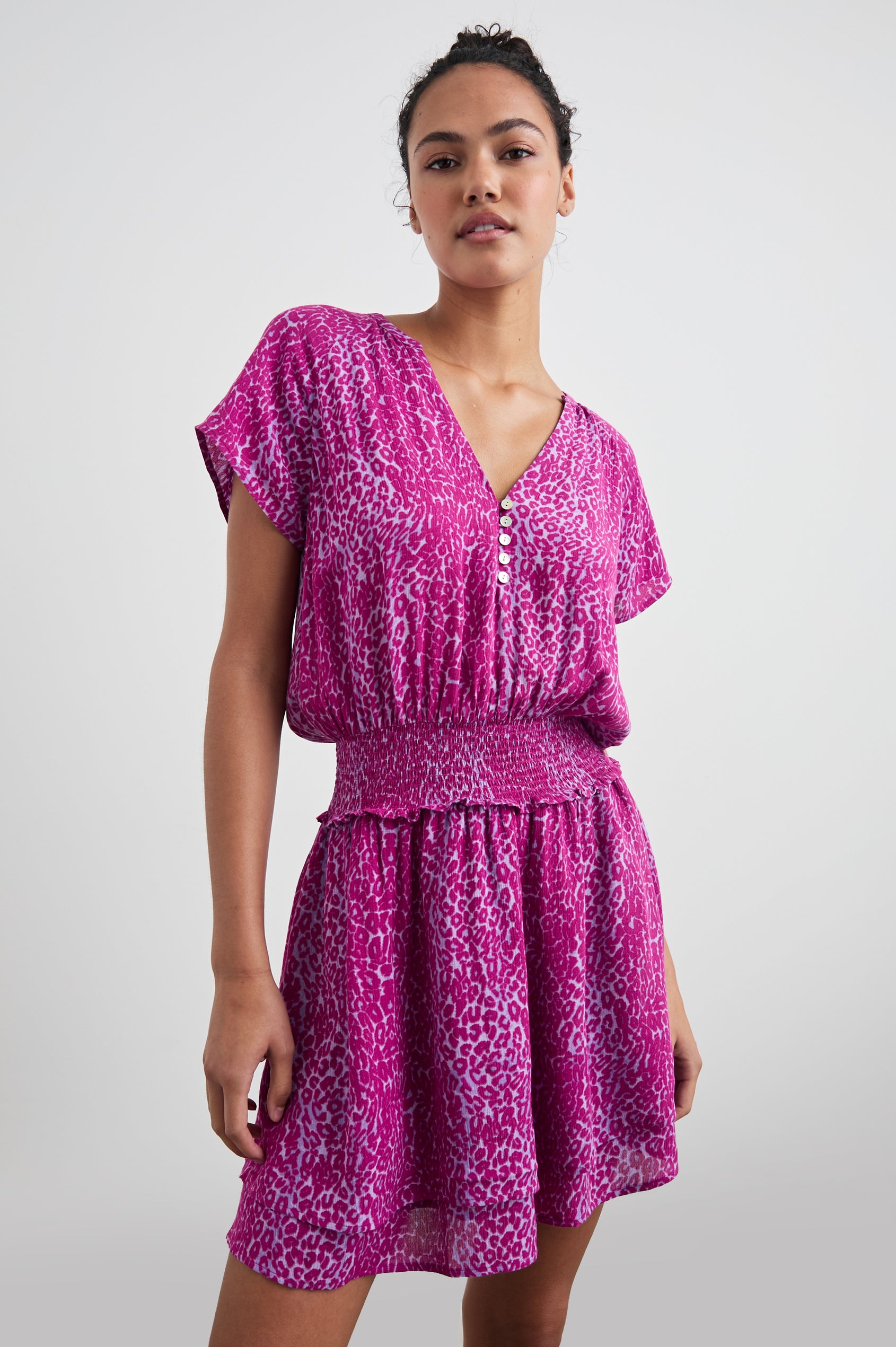 Karla Short Sleeve Mini Dress with a V Neck with Four Buttons, a Shirred Waist and a Double-Layered Skirt in Magenta Cheetah Colorway, Magenta Spots on White - Front View Featured on Model
