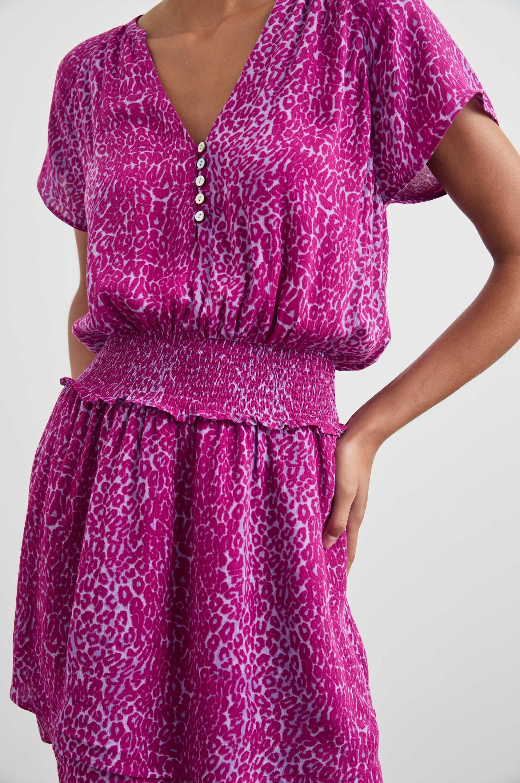 Karla Short Sleeve Mini Dress with a V Neck with Four Buttons, a Shirred Waist and a Double-Layered Skirt in Magenta Cheetah Colorway, Magenta Spots on White - Front View Featured on Model