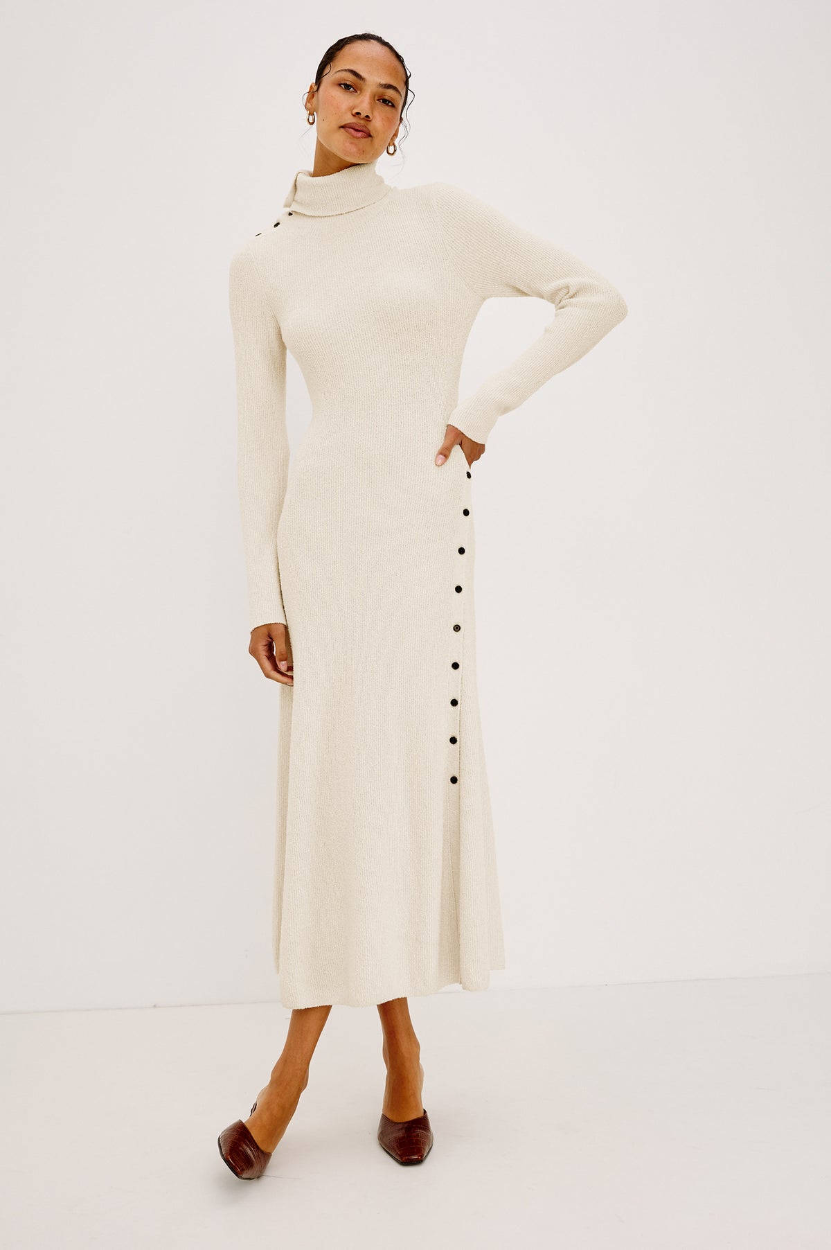 Kat Maxi Dress in Ribbed Cotton Blend With Foldover Turtleneck Button Neckline, Long Sleeves, Fitted Silhouette, Long Sleeves, Side Placket, and Subtle Flare at Hem in Ivory Colorway - Full Body Front View Featured on Model
