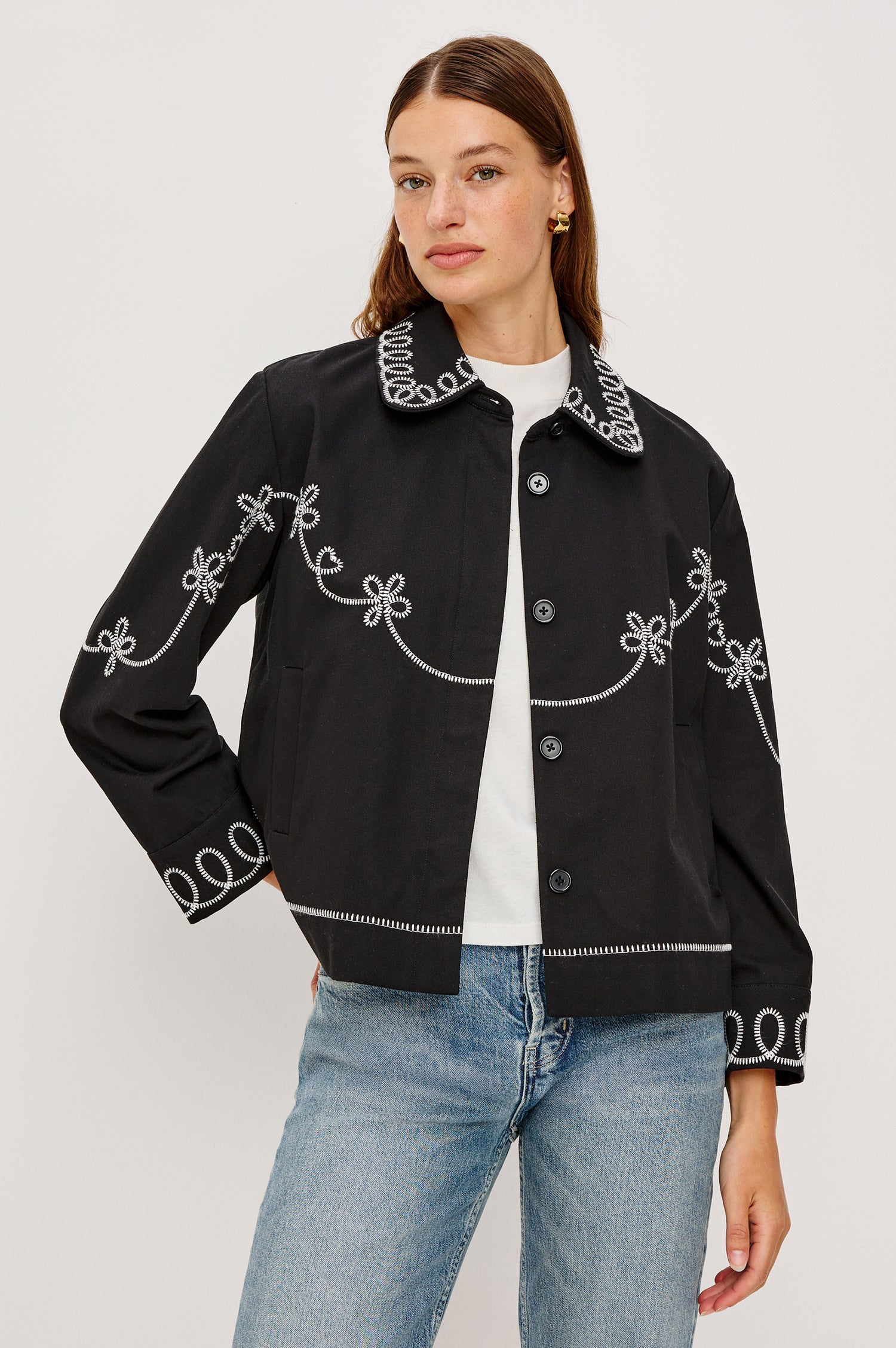 The Keaton is a collared button front jacket with contrast white western inspired embroidery on cuffs, collar, hem, sleeves and bodice in Black colorway. Front view featured on model.