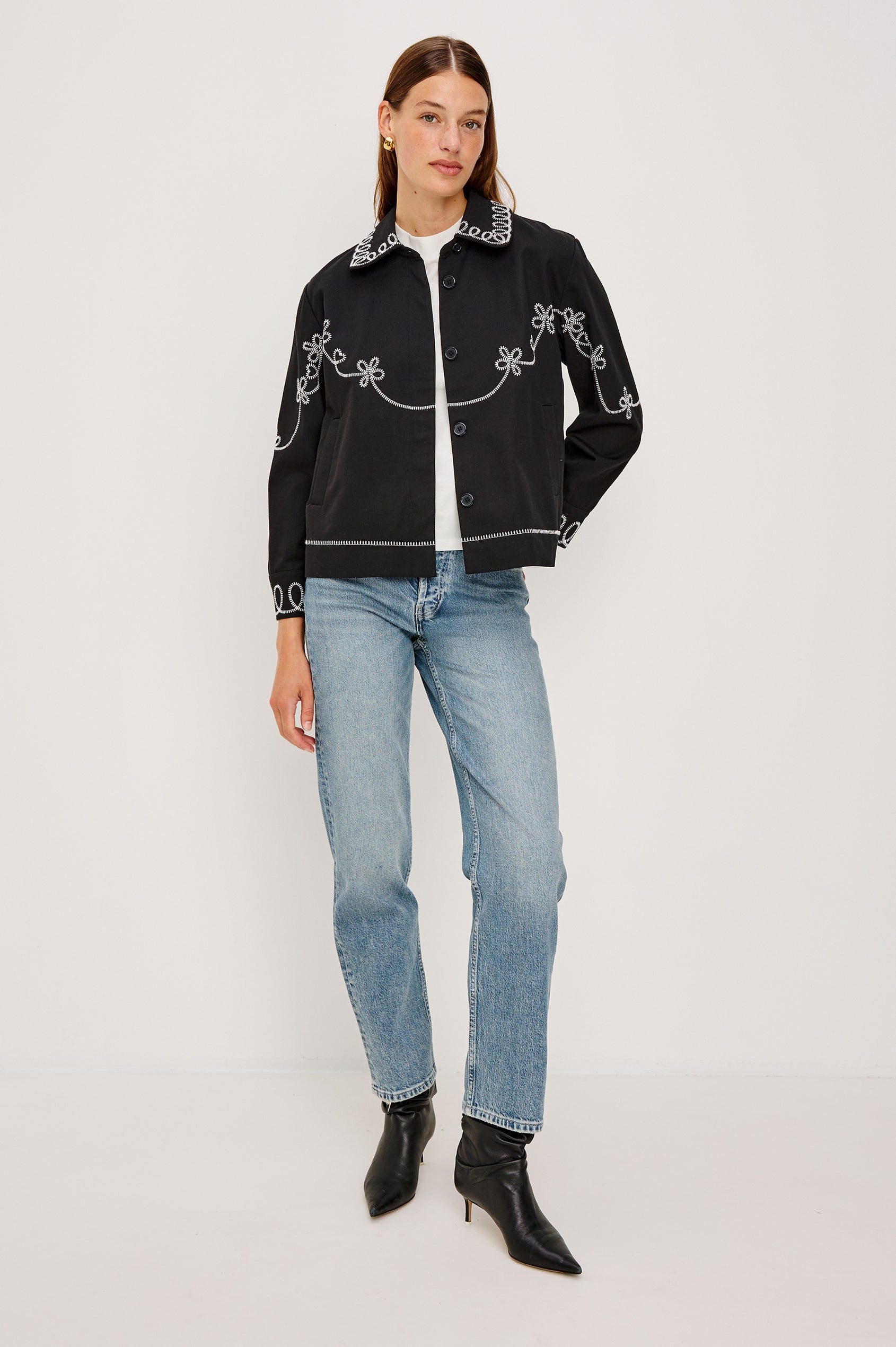 The Keaton is a collared button front jacket with contrast white western inspired embroidery on cuffs, collar, hem, sleeves and bodice in Black colorway. Front full body view featured on model.