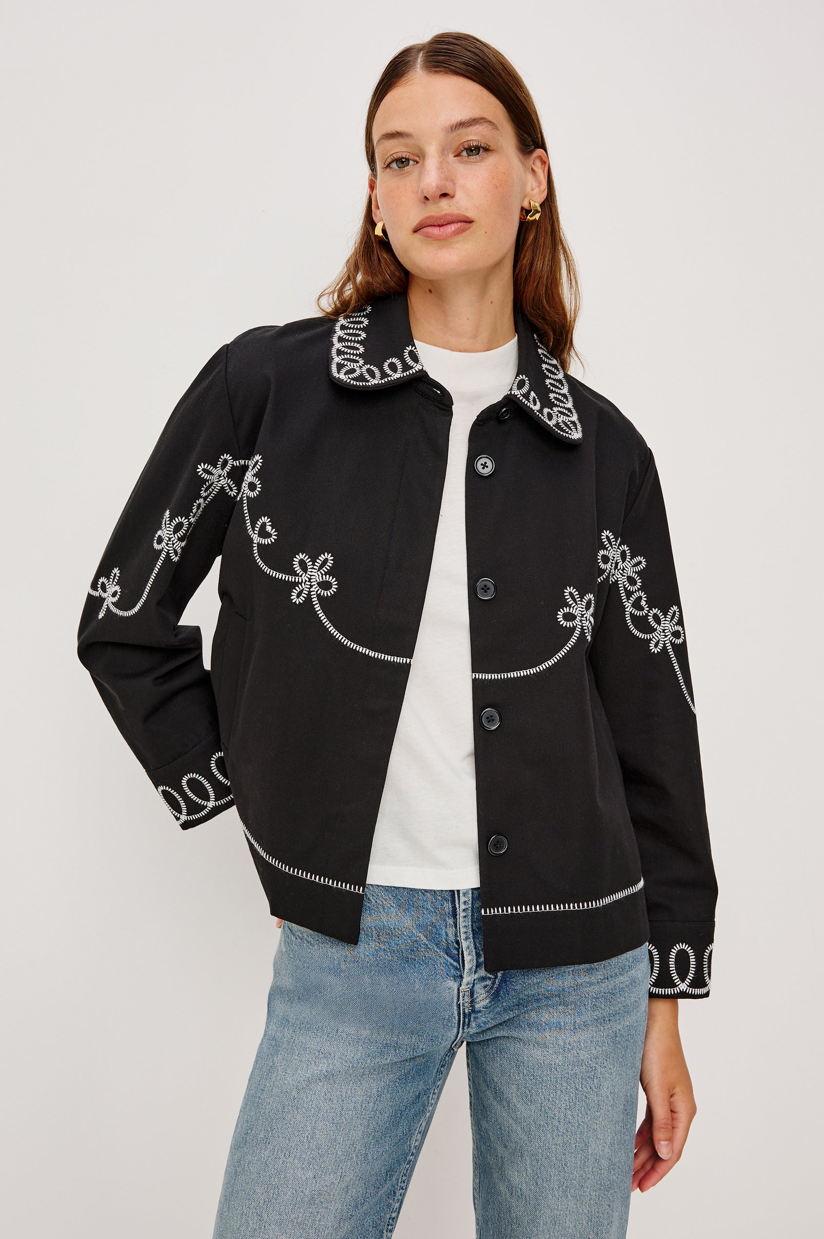 The Keaton is a collared button front jacket with contrast white western inspired embroidery on cuffs, collar, hem, sleeves and bodice in Black colorway. Front view featured on model.