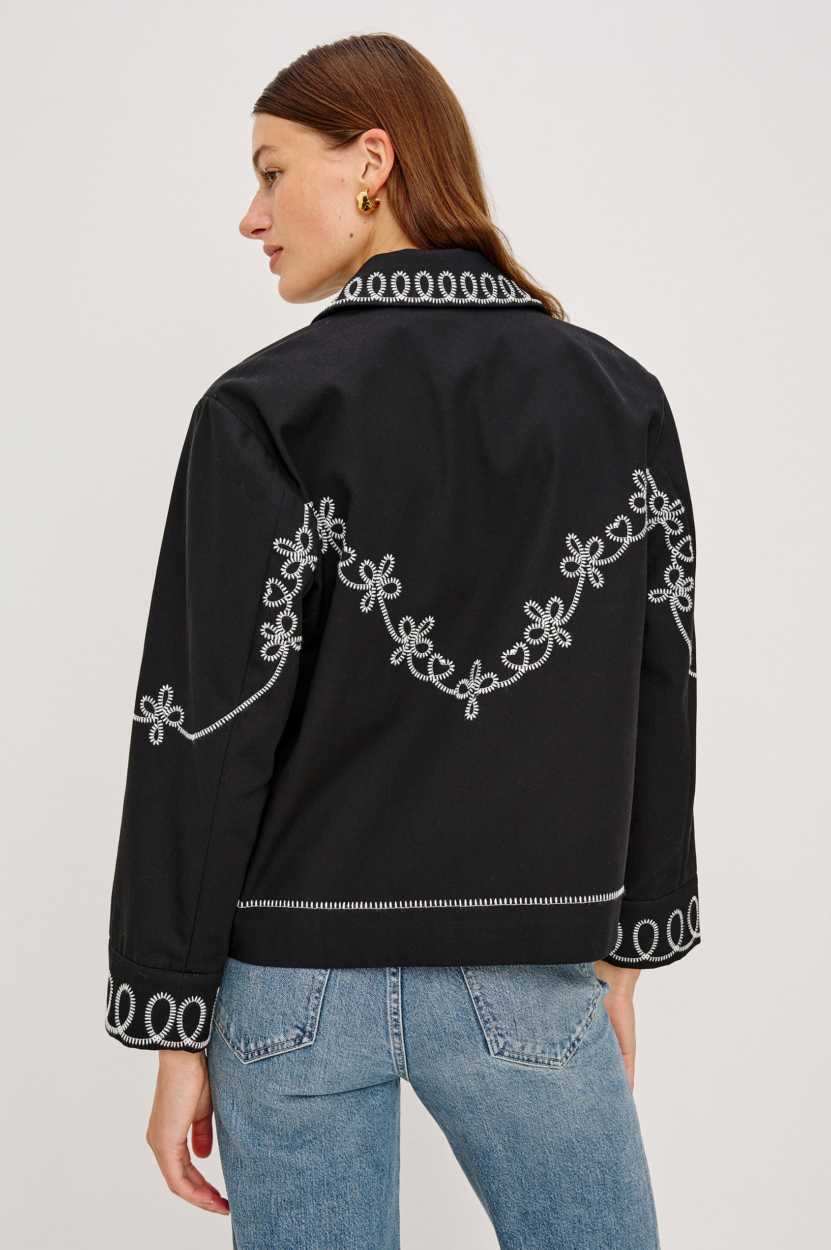 The Keaton is a collared button front jacket with contrast white western inspired embroidery on cuffs, collar, hem, sleeves and bodice in Black colorway. Back view featured on model.