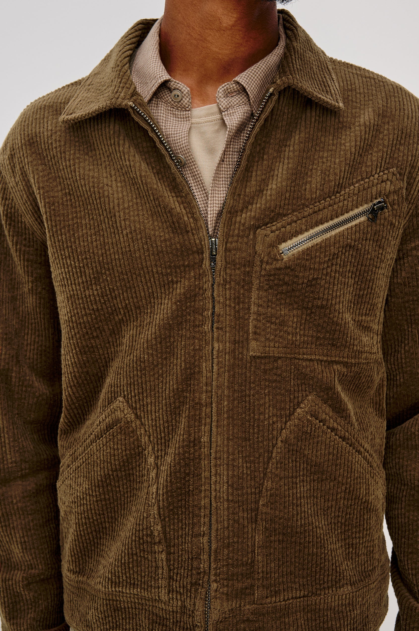 Ketter Zip Up Jacket with Two Curved Front Patch Pockets, a Diagonally Zippered Chest Patch Pocket and Adjustable Button Straps on the Hem in Chicory Colorway, a Warm Brown with Non Contrast Collar - Front Detail View Featured on Model.