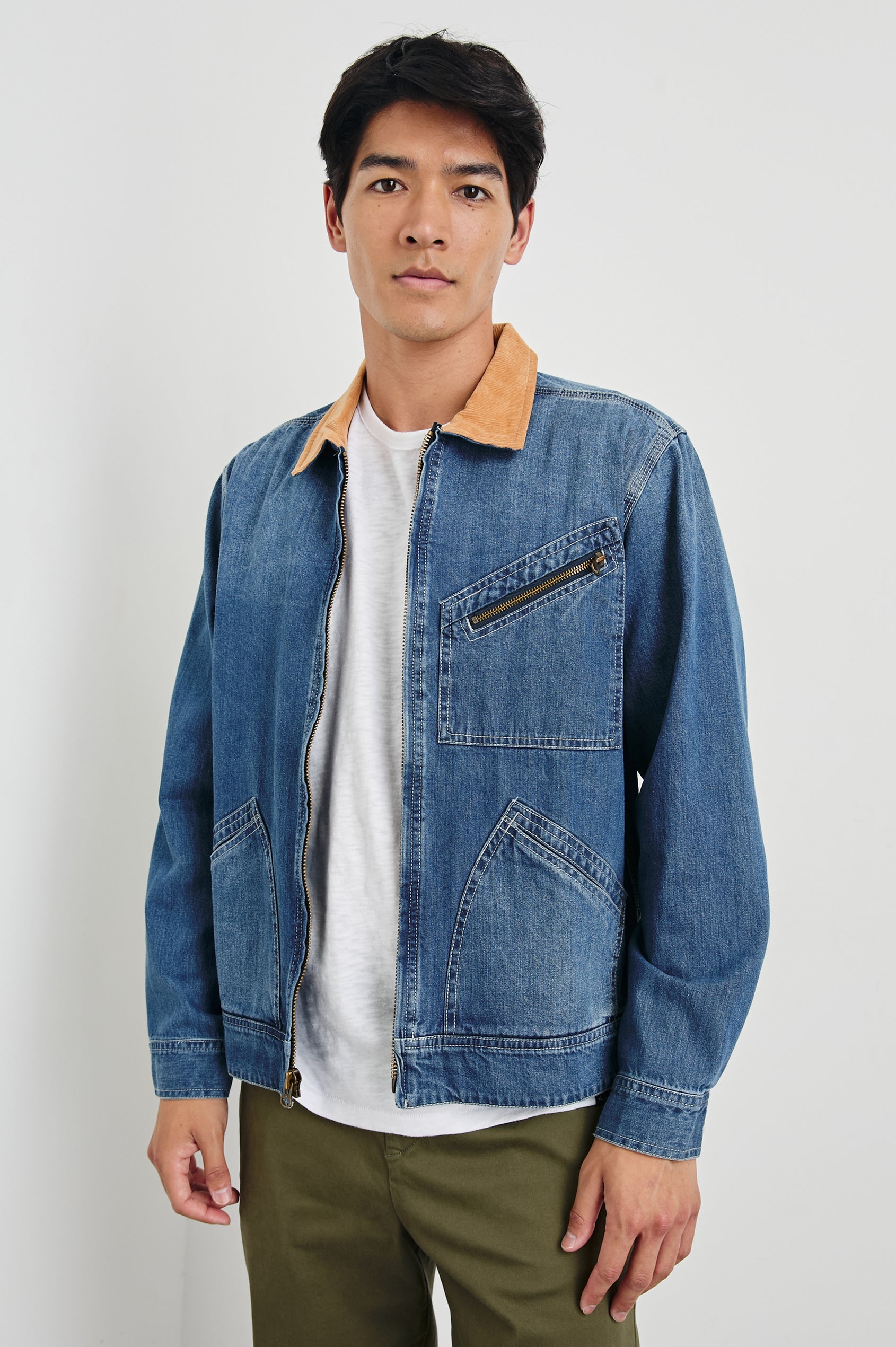 Ketter Zip Up Jacket with Two Curved Front Patch Pockets, a Diagonally Zippered Chest Patch Pocket and Adjustable Button Straps on the Hem in Indigo Patina Wash Colorway, with a Tan Collar - Front View Featured on Model