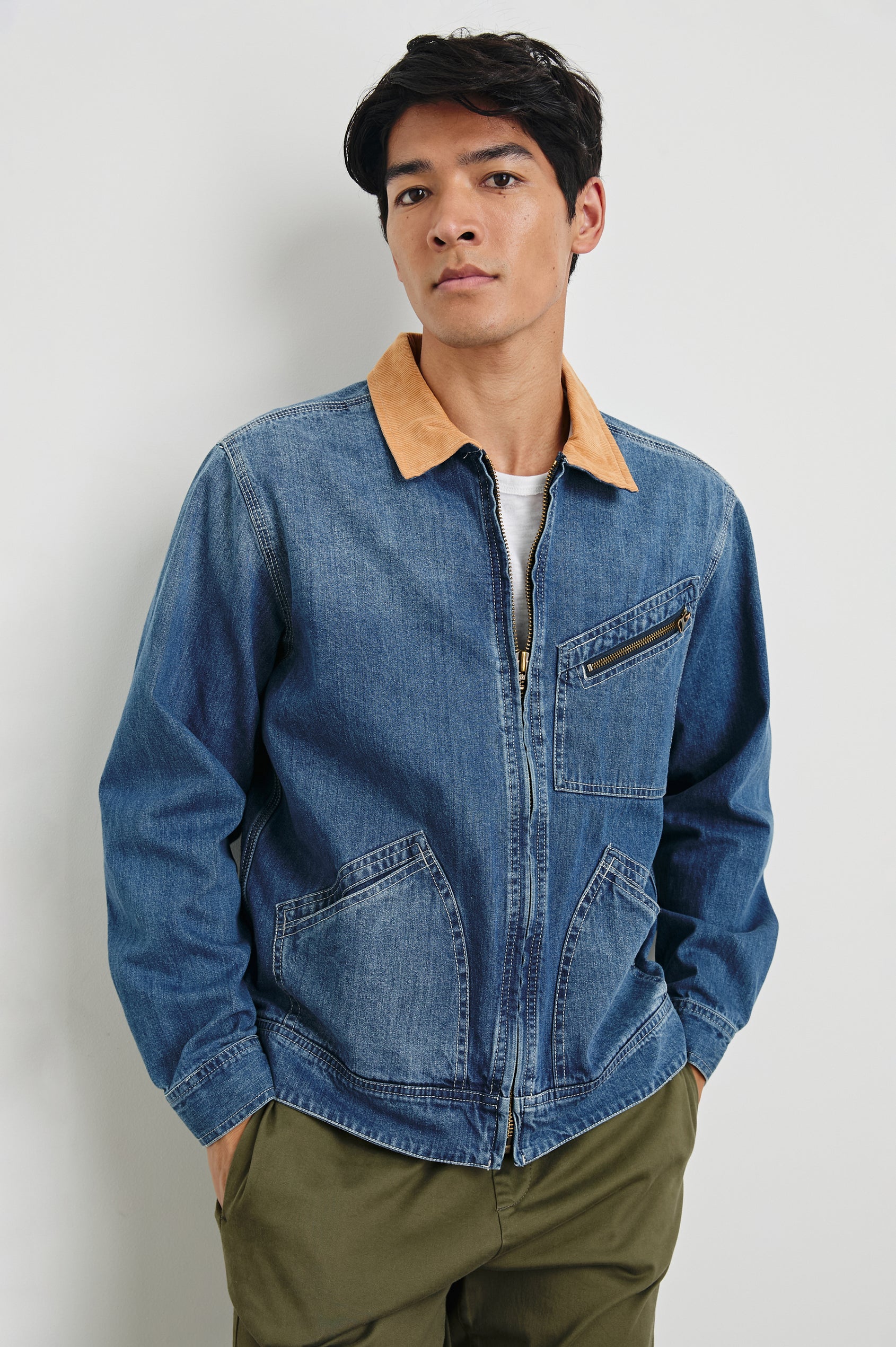Ketter Zip Up Jacket with Two Curved Front Patch Pockets, a Diagonally Zippered Chest Patch Pocket and Adjustable Button Straps on the Hem in Indigo Patina Wash Colorway, with a Tan Collar - Front View Featured on Model