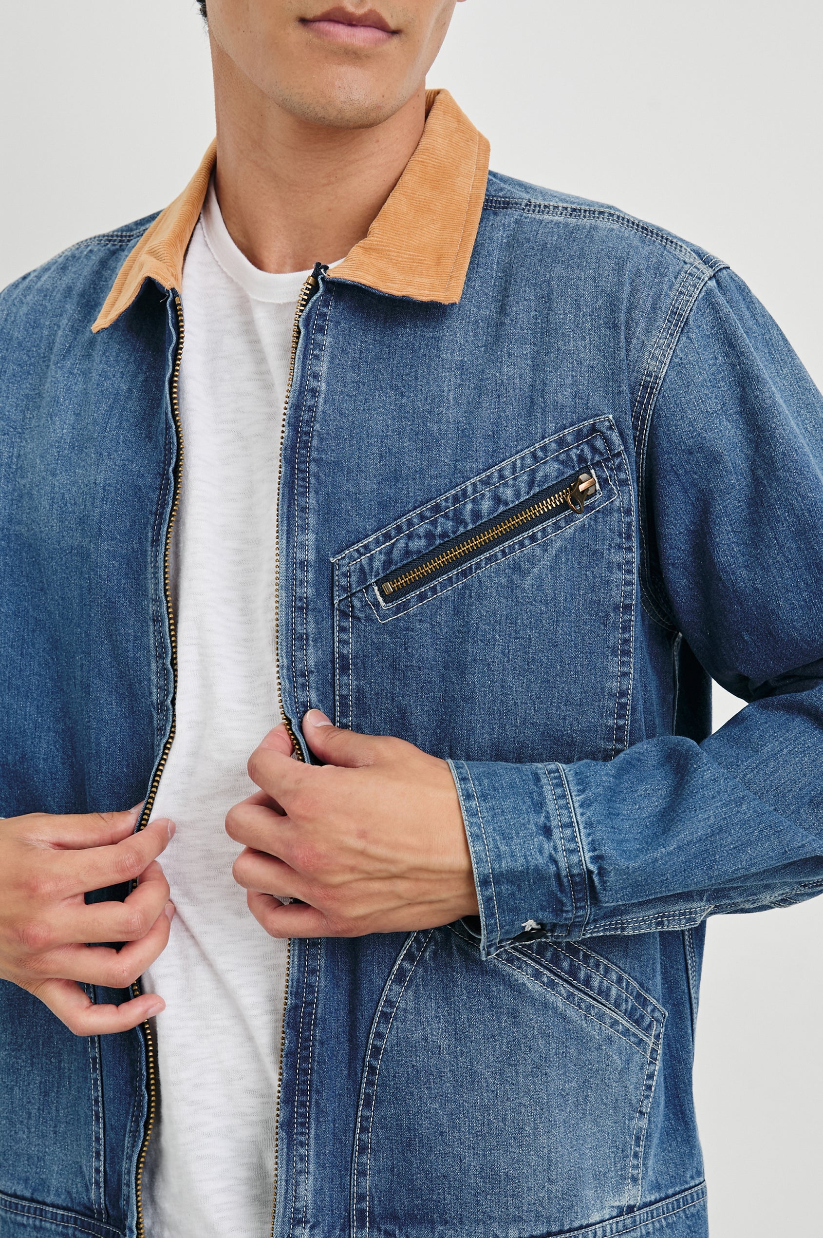 Ketter Zip Up Jacket with Two Curved Front Patch Pockets, a Diagonally Zippered Chest Patch Pocket and Adjustable Button Straps on the Hem in Indigo Patina Wash Colorway, with a Tan Collar - Front View Featured on Model