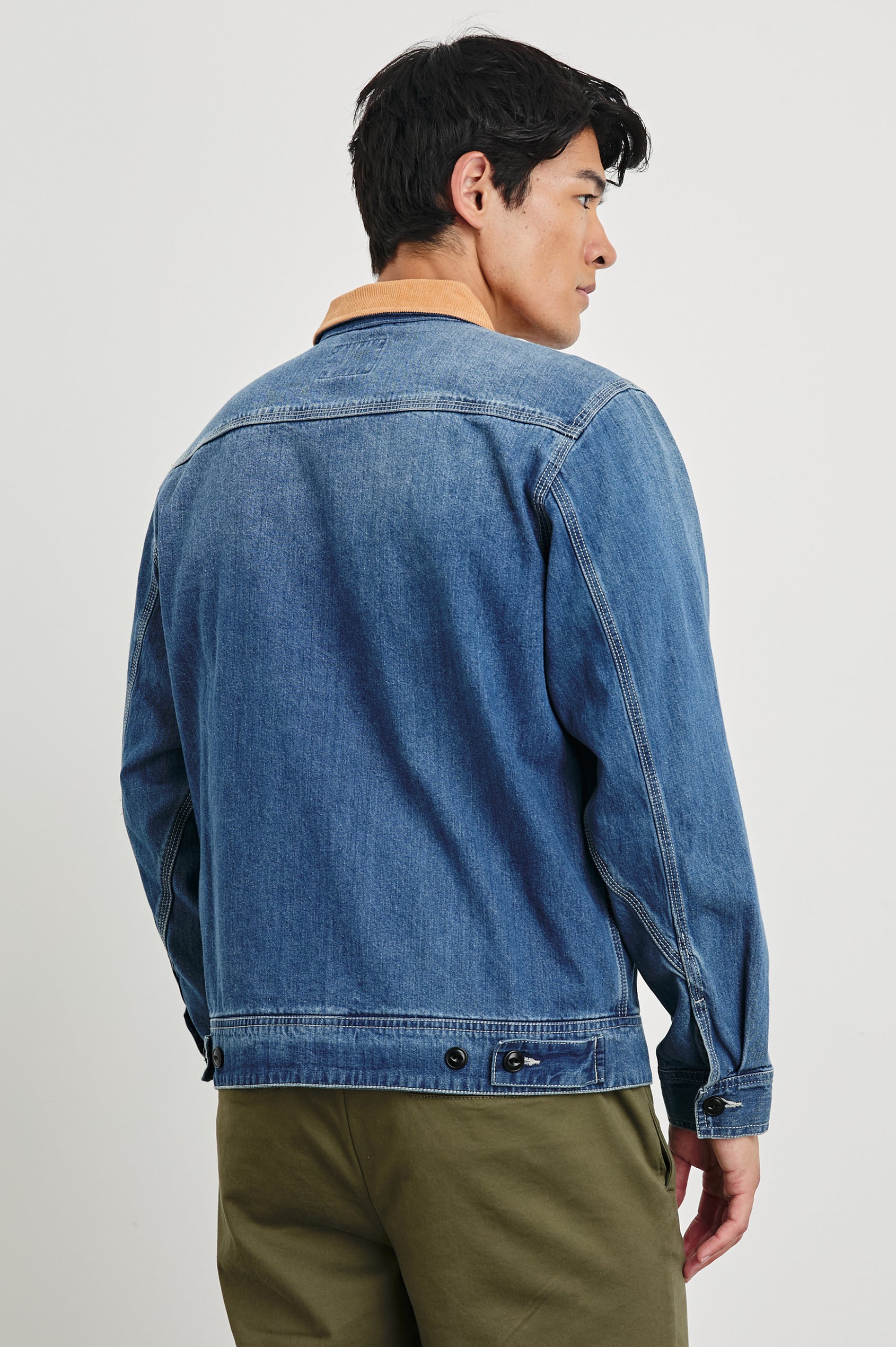 Ketter Zip Up Jacket with Two Curved Front Patch Pockets, a Diagonally Zippered Chest Patch Pocket and Adjustable Button Straps on the Hem in Indigo Patina Wash Colorway, with a Tan Collar - Back View Featured on Model