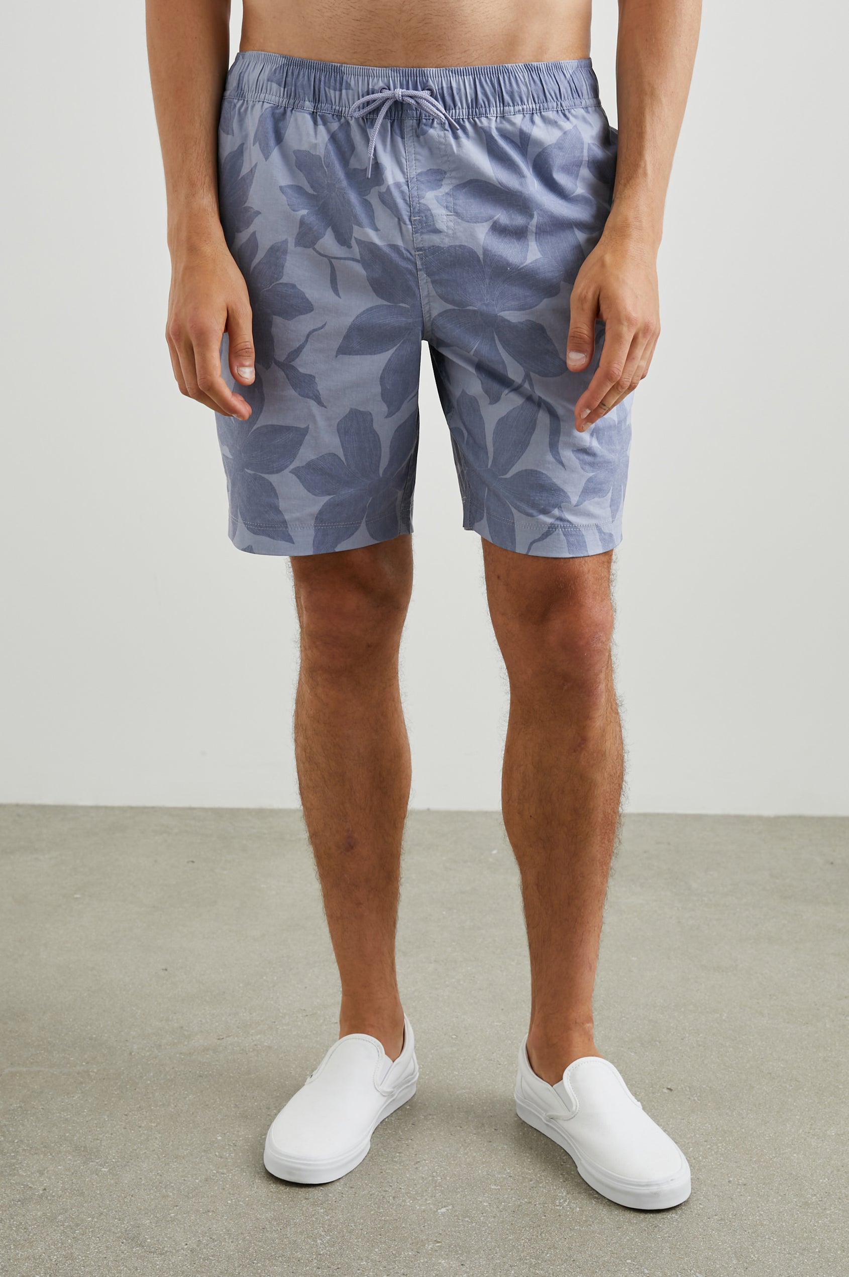 Kian Swim Shorts with an Elastic Drawstring Waistband, Two Front Pockets and a Back Button Flap Pocket in Garden Sands Orchid Colorway, Blue Orchids on Light Blue - Front View Featured on Model