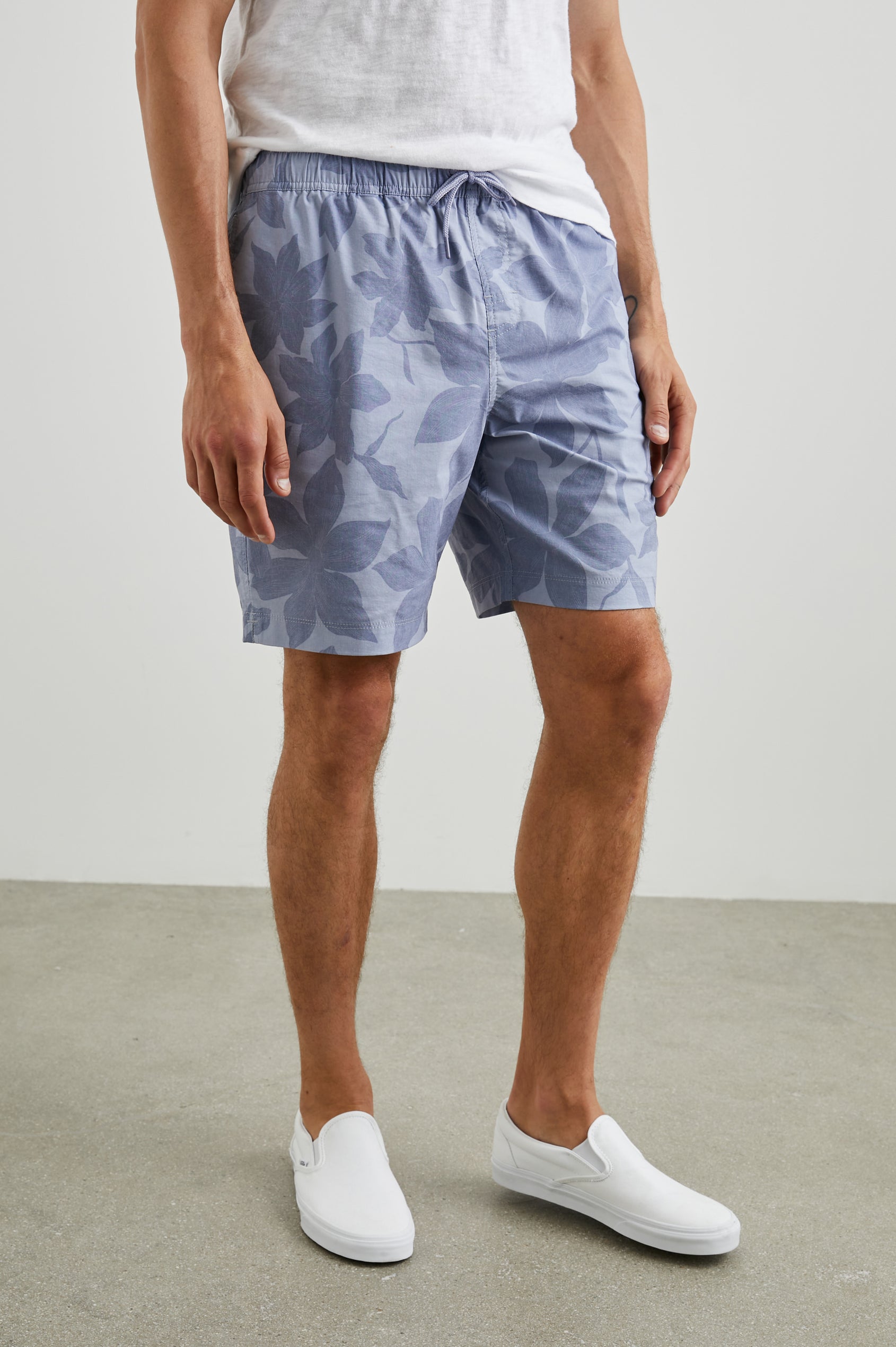 Kian Swim Shorts with an Elastic Drawstring Waistband, Two Front Pockets and a Back Button Flap Pocket in Garden Sands Orchid Colorway, Blue Orchids on Light Blue - Front View Featured on Model