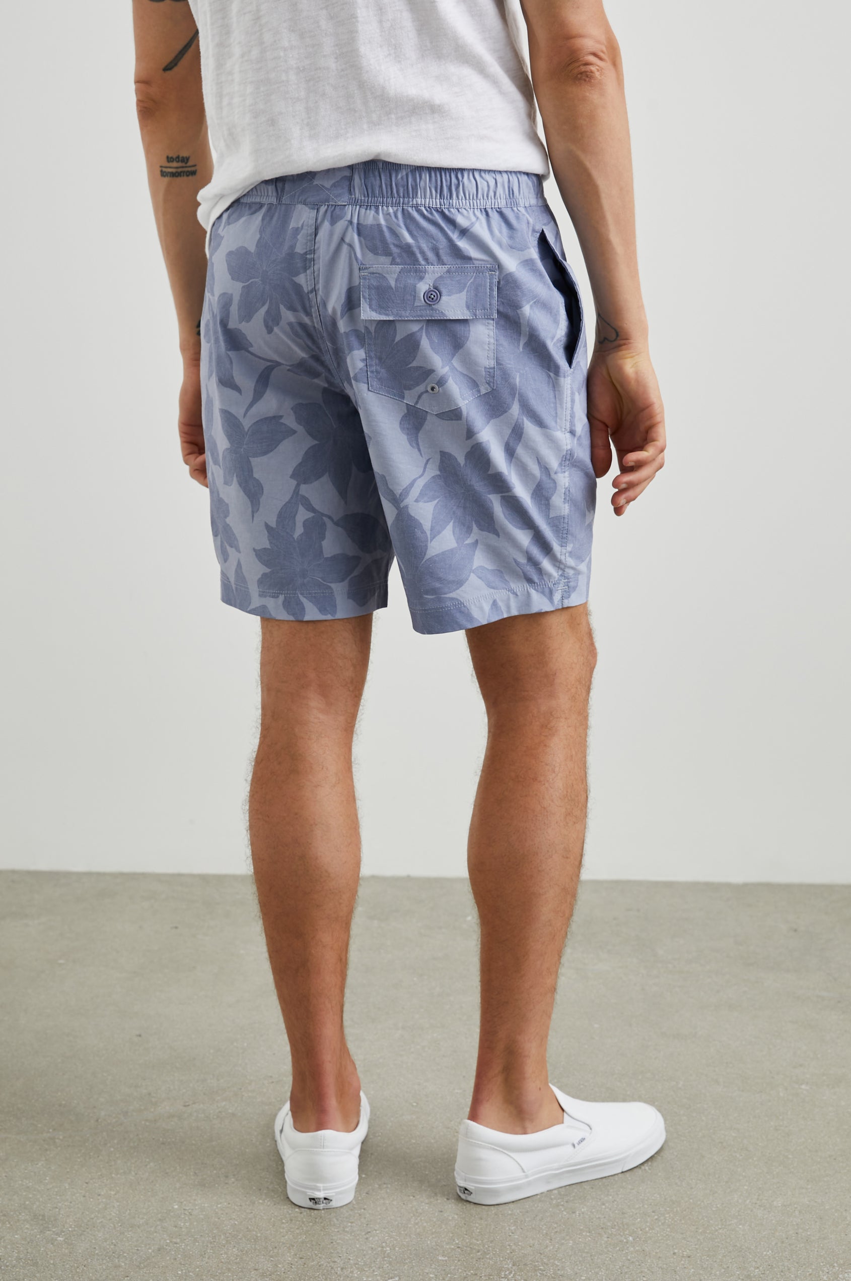 Kian Swim Shorts with an Elastic Drawstring Waistband, Two Front Pockets and a Back Button Flap Pocket in Garden Sands Orchid Colorway, Blue Orchids on Light Blue - Back View Featured on Model
