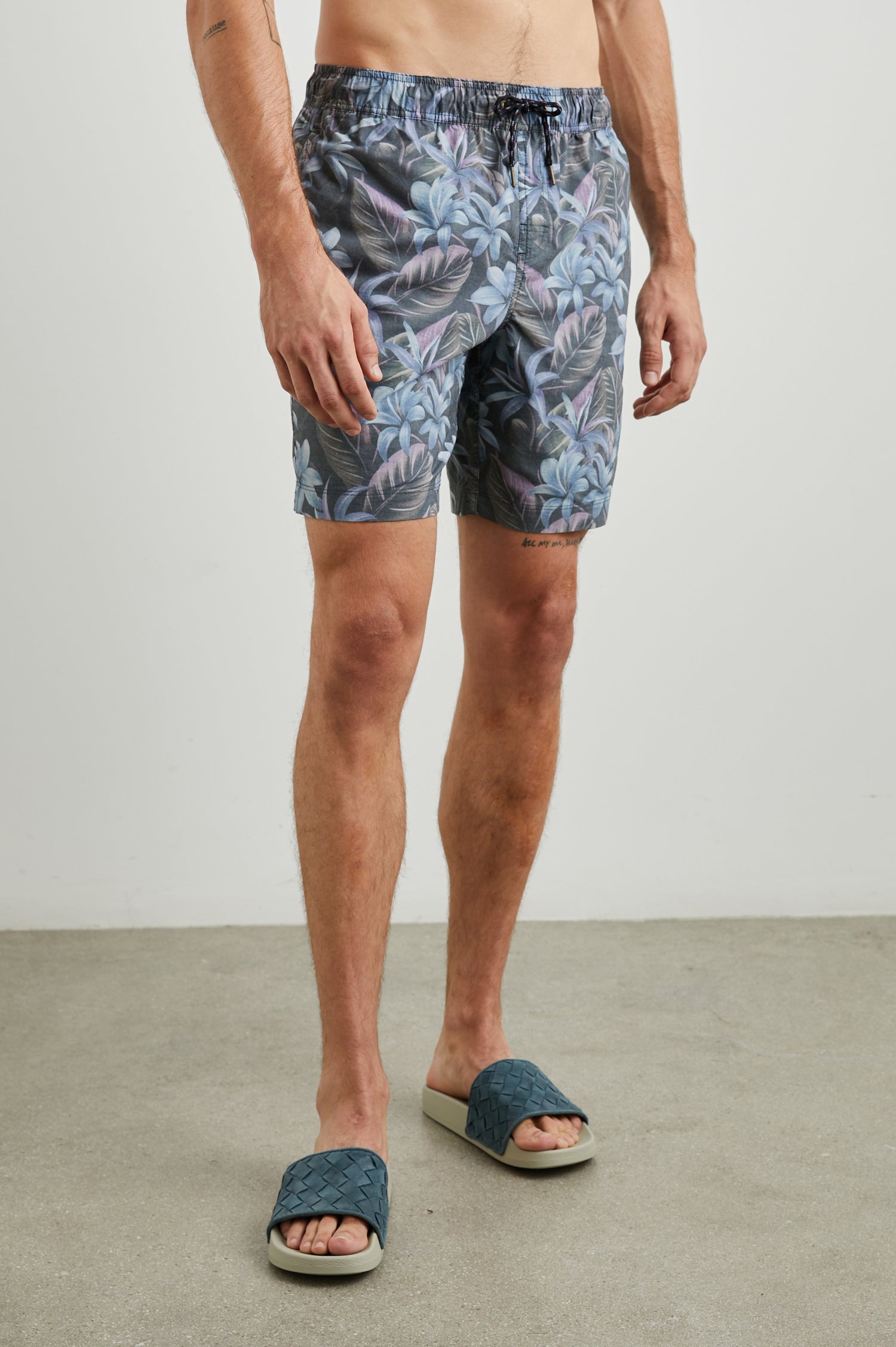 Kian Swim Shorts with an Elastic Drawstring Waistband, Two Front Pockets and a Back Button Flap Pocket in Jungle Garden Midnight Colorway, Plants on muted Pinks, blues and Greens on Black - Front View Featured on Model