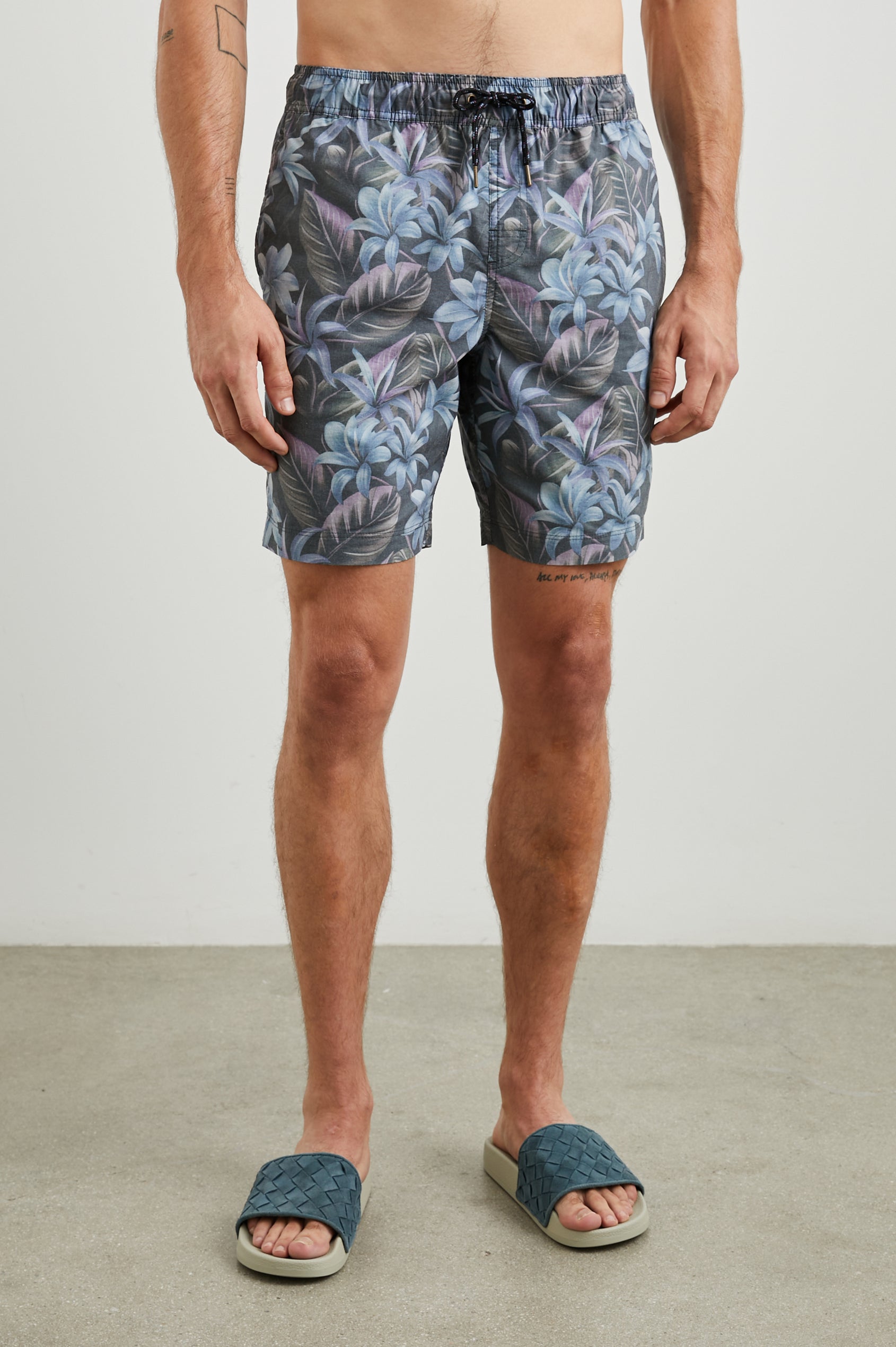 Kian Swim Shorts with an Elastic Drawstring Waistband, Two Front Pockets and a Back Button Flap Pocket in Jungle Garden Midnight Colorway, Plants on muted Pinks, blues and Greens on Black - Front View Featured on Model