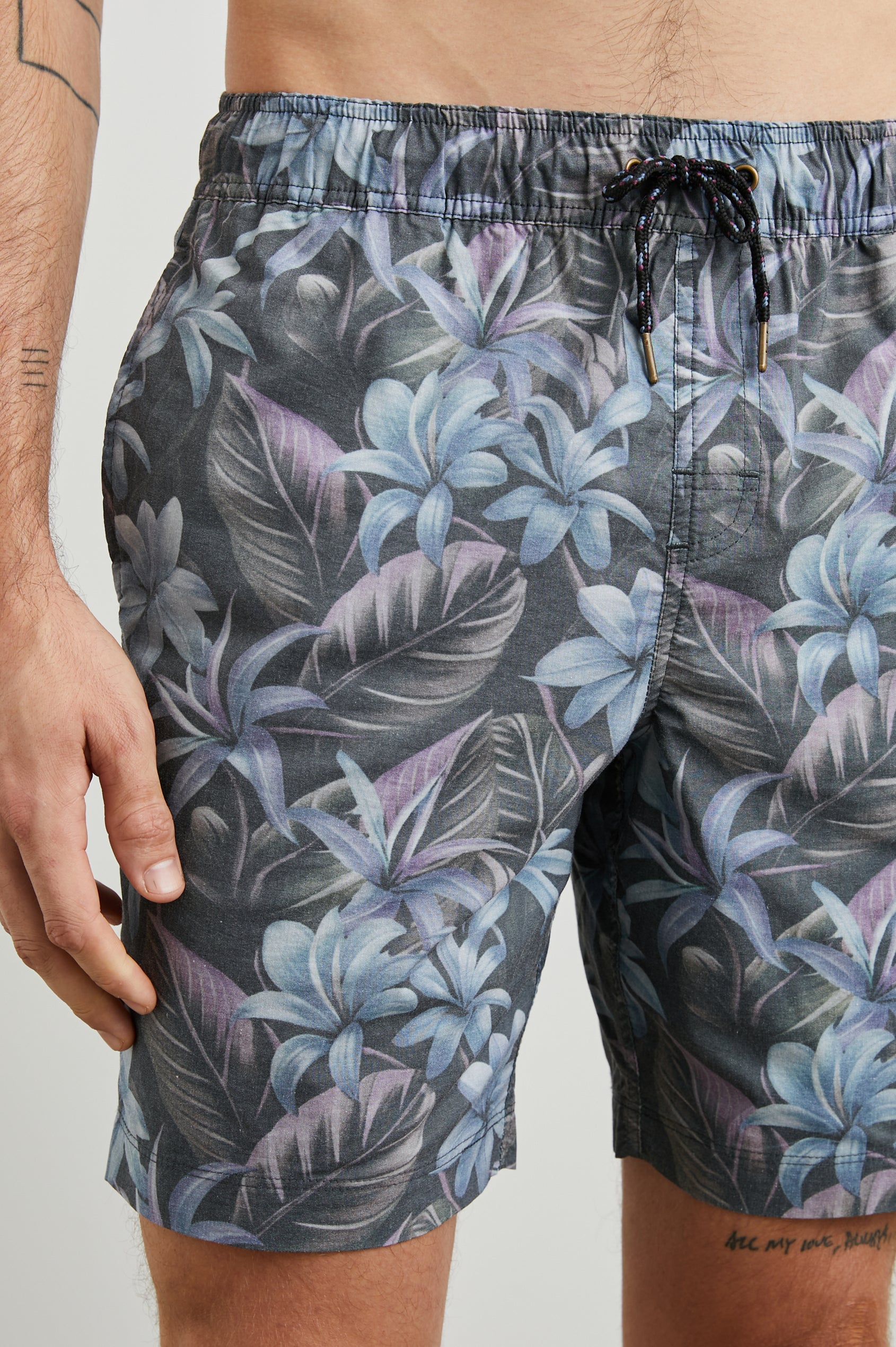 Kian Swim Shorts with an Elastic Drawstring Waistband, Two Front Pockets and a Back Button Flap Pocket in Jungle Garden Midnight Colorway, Plants on muted Pinks, blues and Greens on Black - Front View Featured on Model