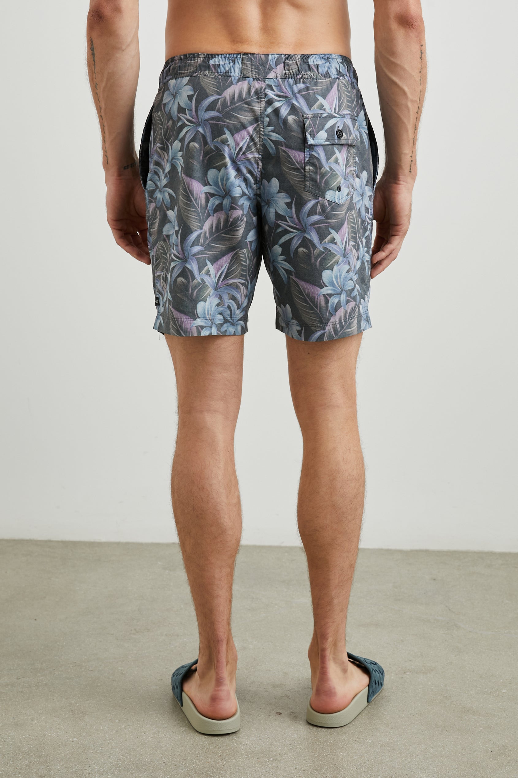 Kian Swim Shorts with an Elastic Drawstring Waistband, Two Front Pockets and a Back Button Flap Pocket in Jungle Garden Midnight Colorway, Plants on muted Pinks, blues and Greens on Black - Back View Featured on Model