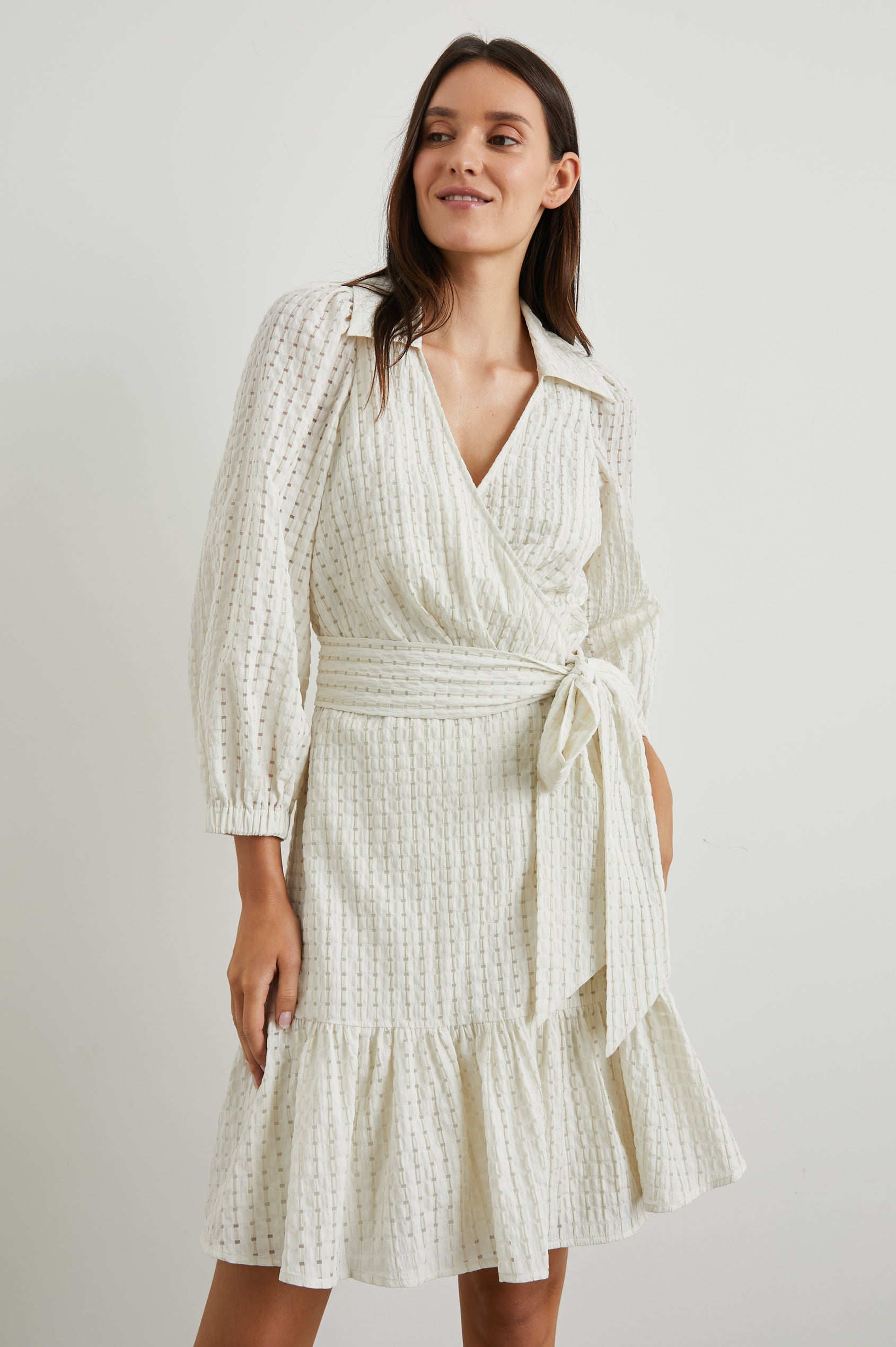 Kiara Mini Dress with Three-Quarter Sleeves, a Fabric Waist Tie, a Deep V Neck, a Collar, a Ruffled Hem and Textured Fabric in Ivory Seersucker Colorway - Front View Featured on Model 