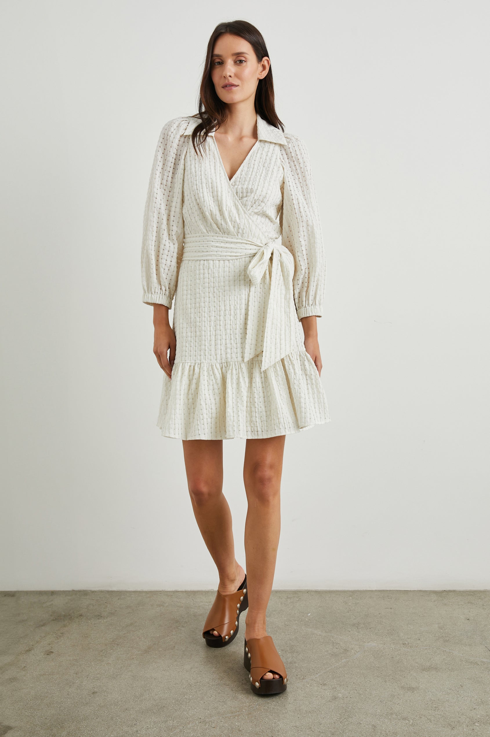 Kiara Mini Dress with Three-Quarter Sleeves, a Fabric Waist Tie, a Deep V Neck, a Collar, a Ruffled Hem and Textured Fabric in Ivory Seersucker Colorway - Front Full Body View Featured on Model 