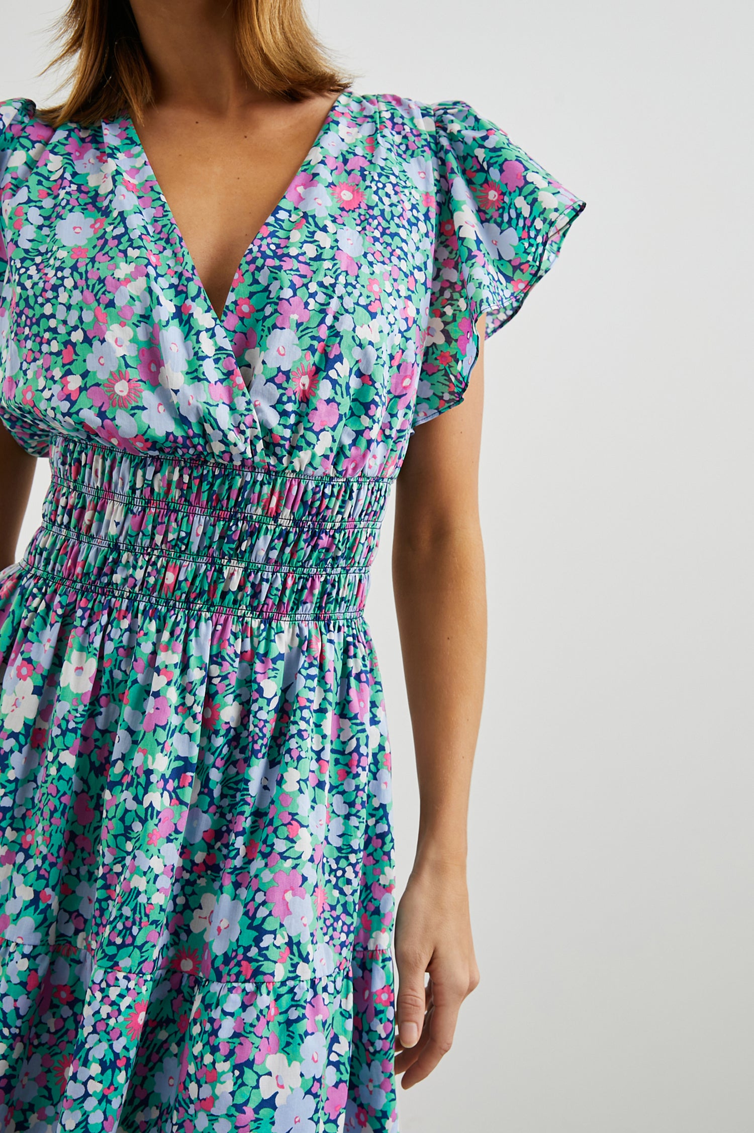 Kimora Above-Knee Dress with Flutter Sleeves, a V Neckline, a Cinched Waist and a Tiered Skirt in Navy Leilani Floral Colorway with flowers in pinks, purples and greens - Front View Featured on Model