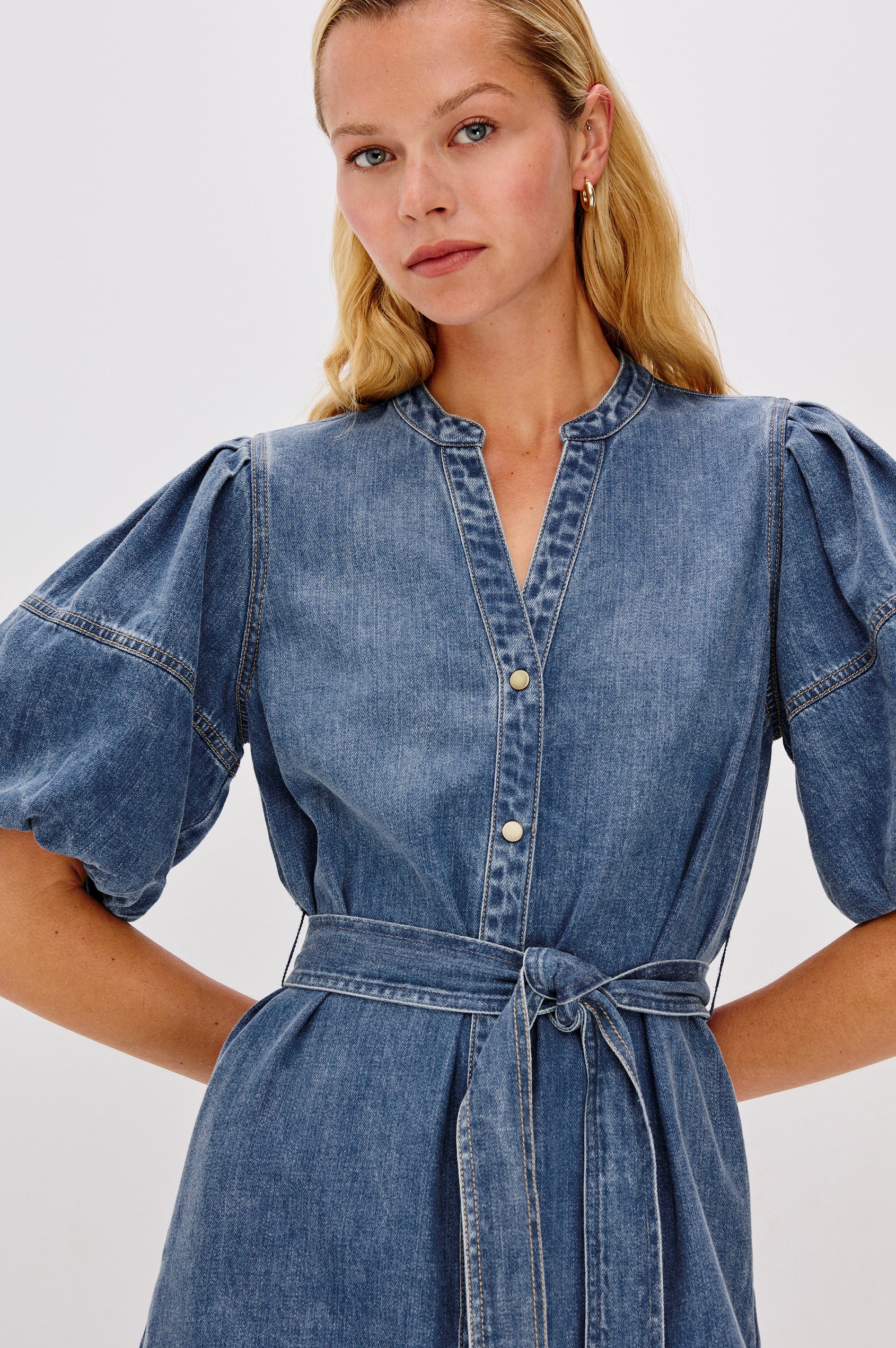 Kingsley Denim Mini Dress with Elbow-Length Puff Sleeves, a V Neck, Snaps Down the Front and a Fabric Tie Belt in Antique Blue Colorway - close up view of details on model