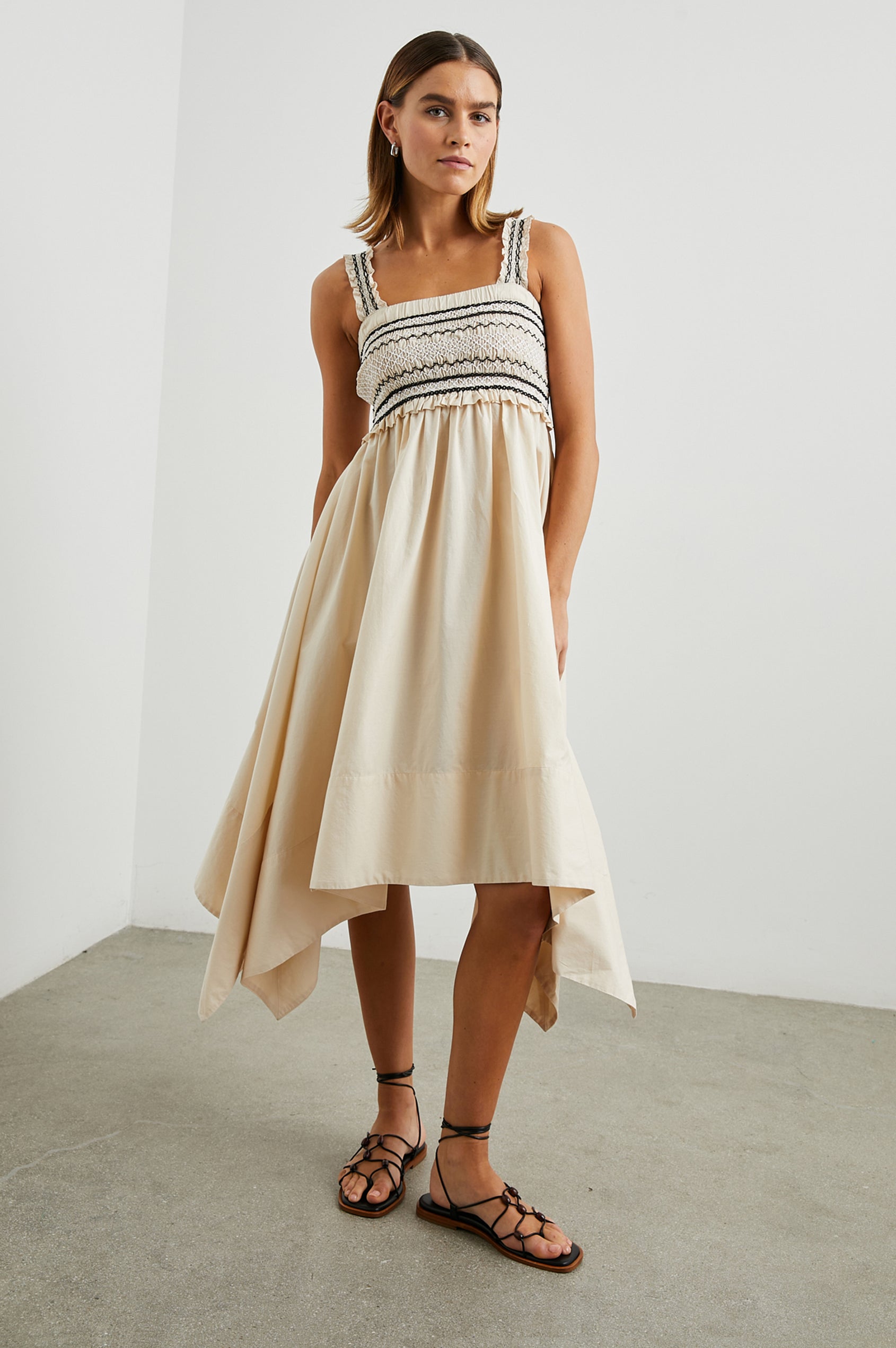 Kirsten Sleeveless Midi Dress with an Asymmetrical Hem, a Square Neckline, Shoulder Straps, a Shirred Bodice, Ruffled Trim on the Bodice, Black and White Stitching Details on the Bodice in Flax Colorway - Front Full Body View Featured on Model 
