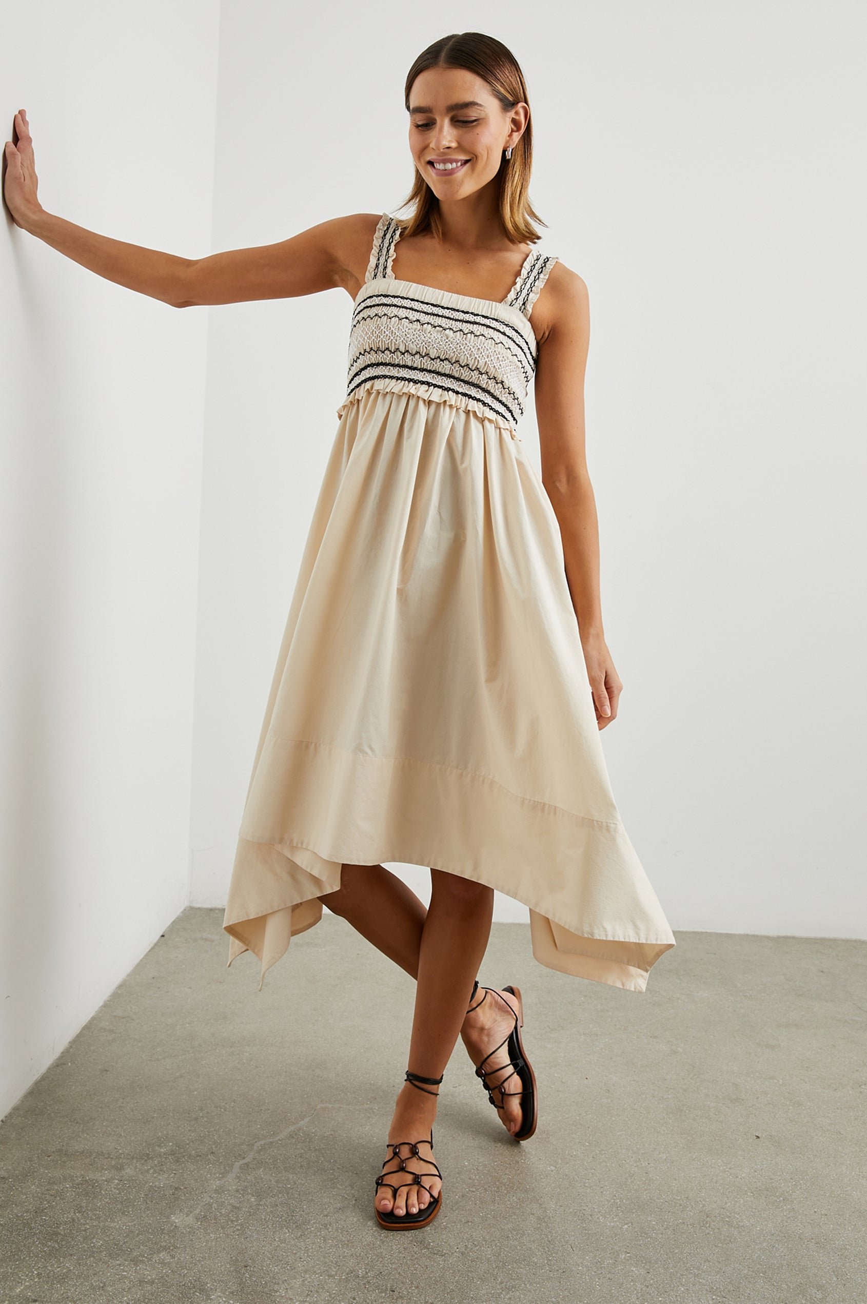 Kirsten Sleeveless Midi Dress with an Asymmetrical Hem, a Square Neckline, Shoulder Straps, a Shirred Bodice, Ruffled Trim on the Bodice, Black and White Stitching Details on the Bodice in Flax Colorway - Front Full Body View Featured on Model 