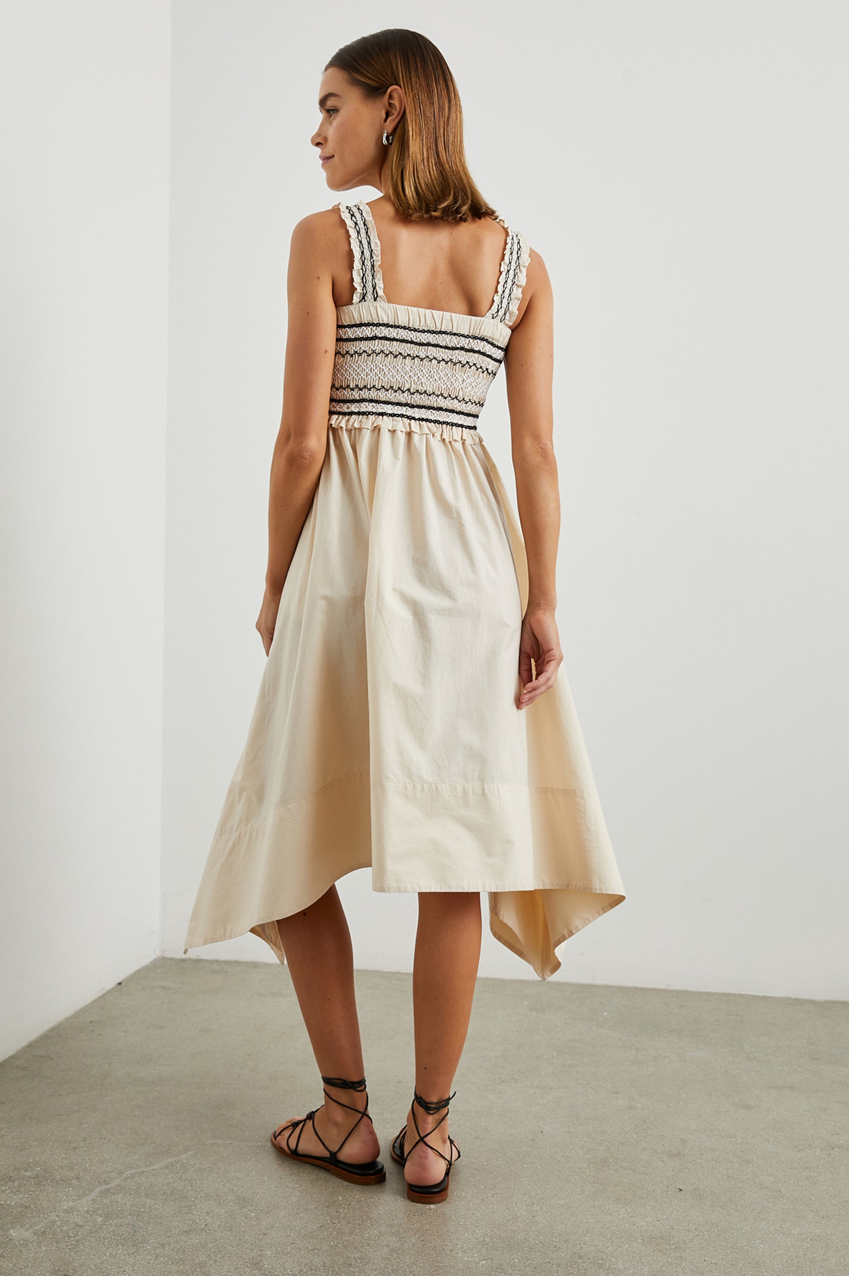 Kirsten Sleeveless Midi Dress with an Asymmetrical Hem, a Square Neckline, Shoulder Straps, a Shirred Bodice, Ruffled Trim on the Bodice, Black and White Stitching Details on the Bodice in Flax Colorway - Back Full Body View Featured on Model 