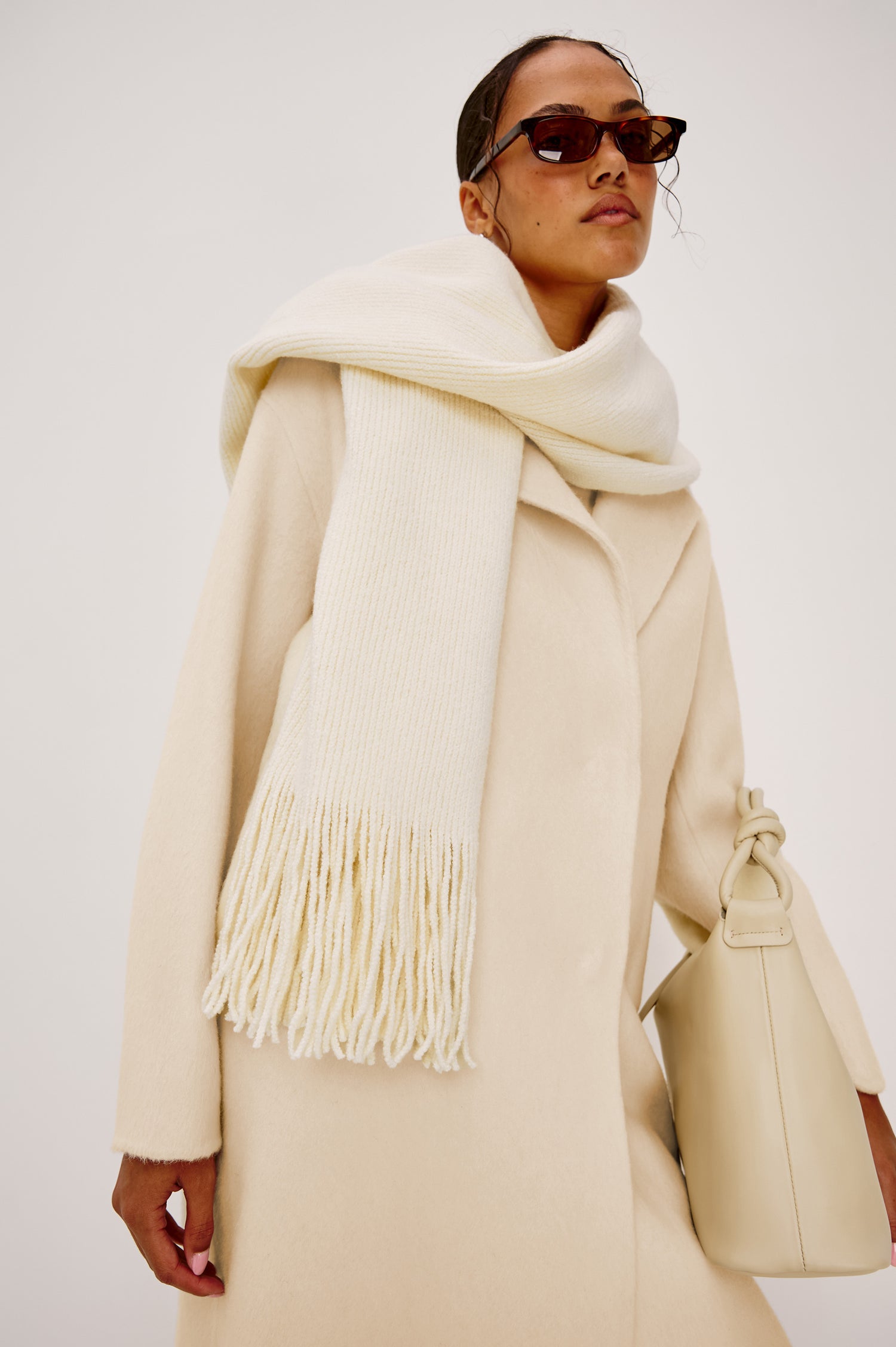Koa oversized knit scarf in ivory with long fringe tassels at the ends. Front view of model featured.