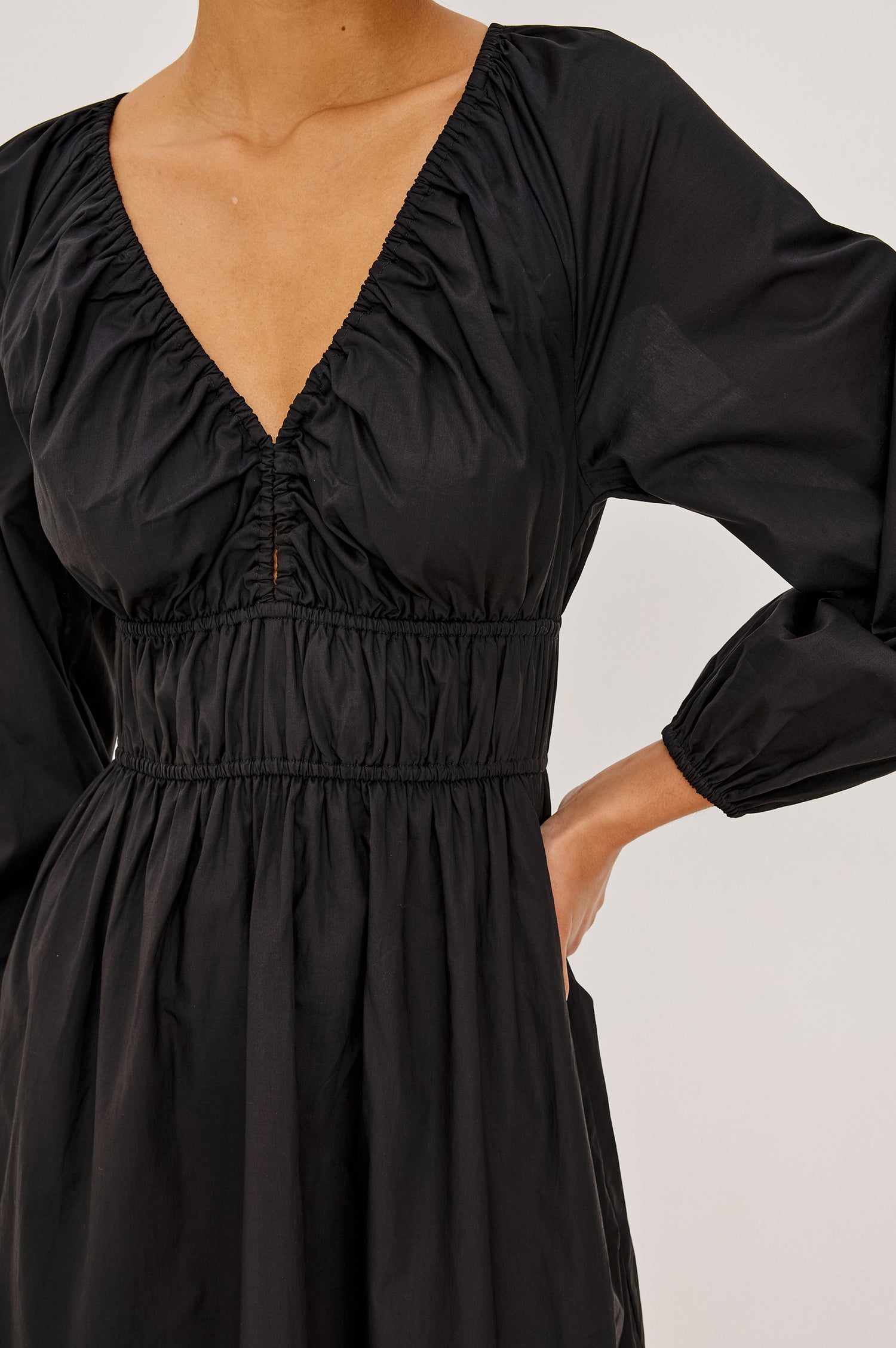 Krina Mini Dress in Cotton Poplin With Deep V-Neckline, Center Front Ties, Long Billowing Sleeves, and Tiered Hem in Black Colorway - Upper Body Front Close Up View Featured on Model