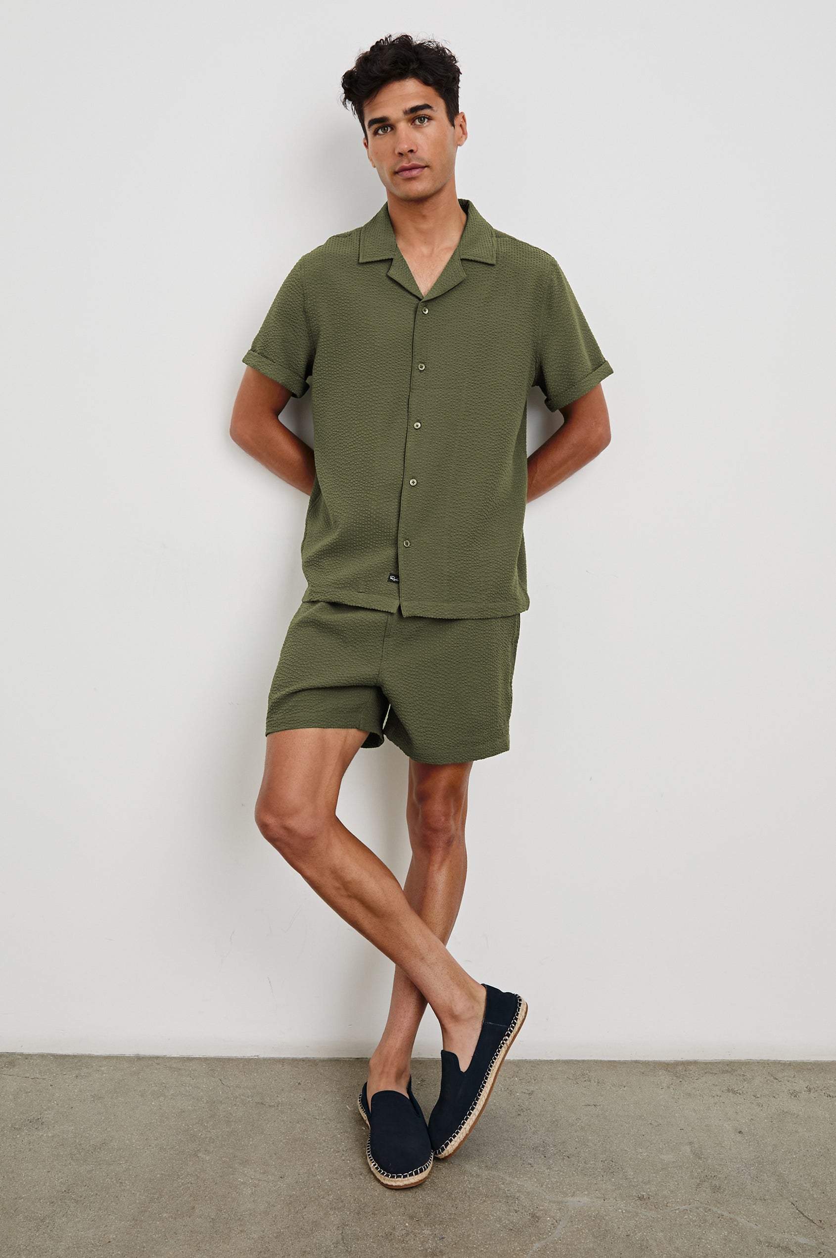 La Brea textured mid-length swim short with adjustable waist drawstring in Olive Seersucker - full body front view on model, posing against wall