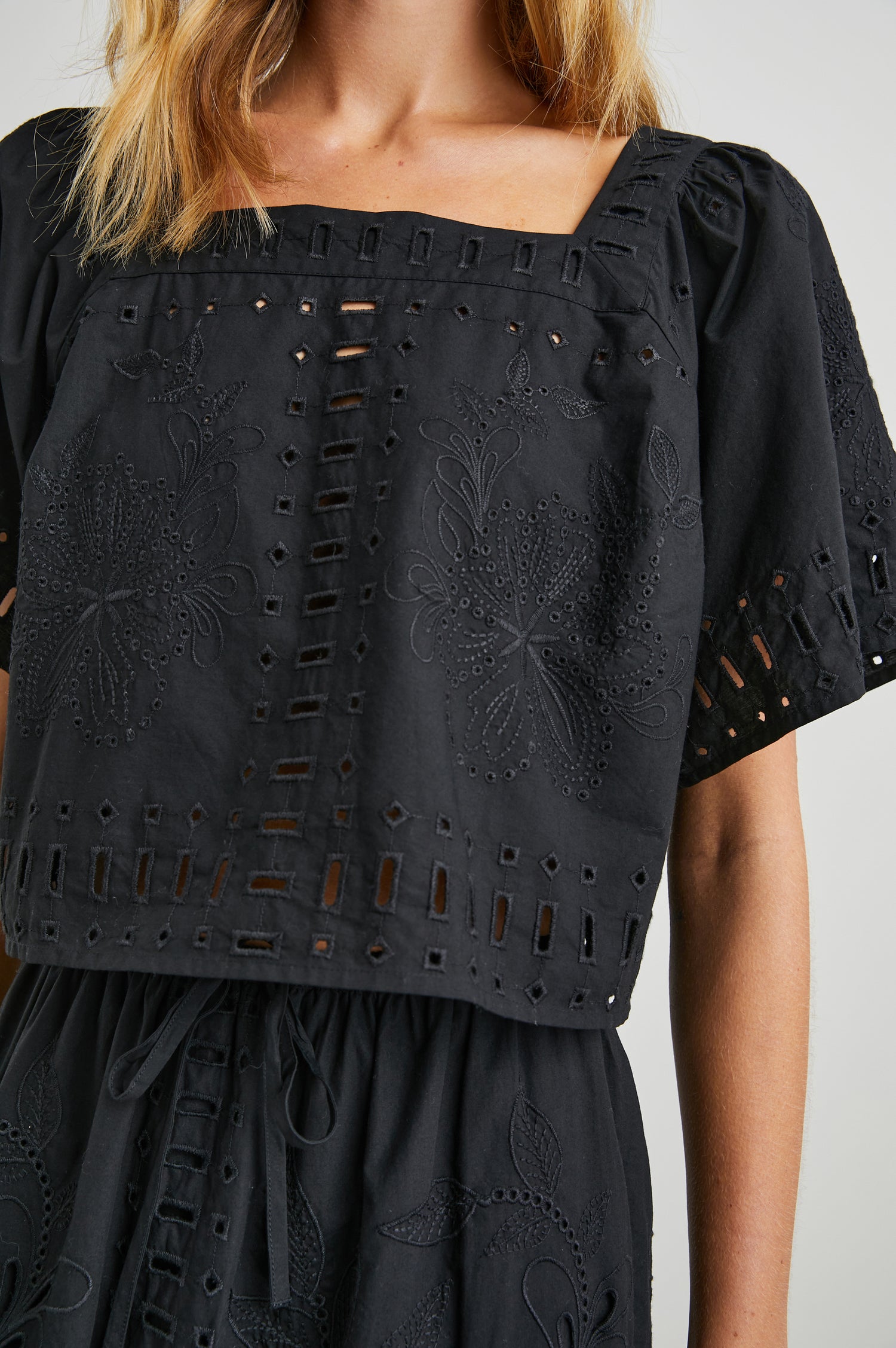 Laine Short Sleeve Crop Top with Square Neckline, and a Floral and Geometric Eyelet Design in Black Colorway - Front View Featured on Model