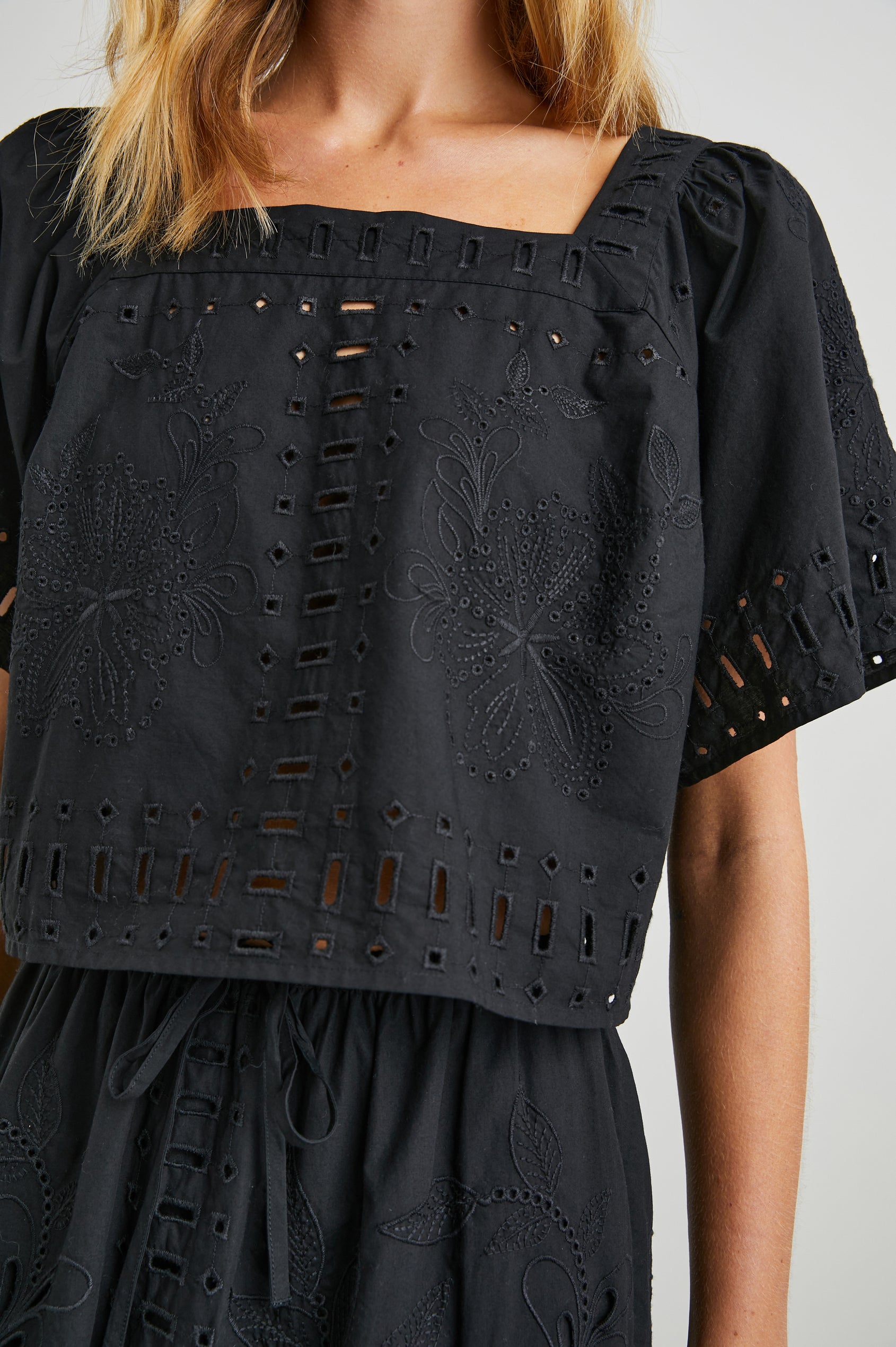 Laine Short Sleeve Crop Top with Square Neckline, and a Floral and Geometric Eyelet Design in Black Colorway - Front View Featured on Model