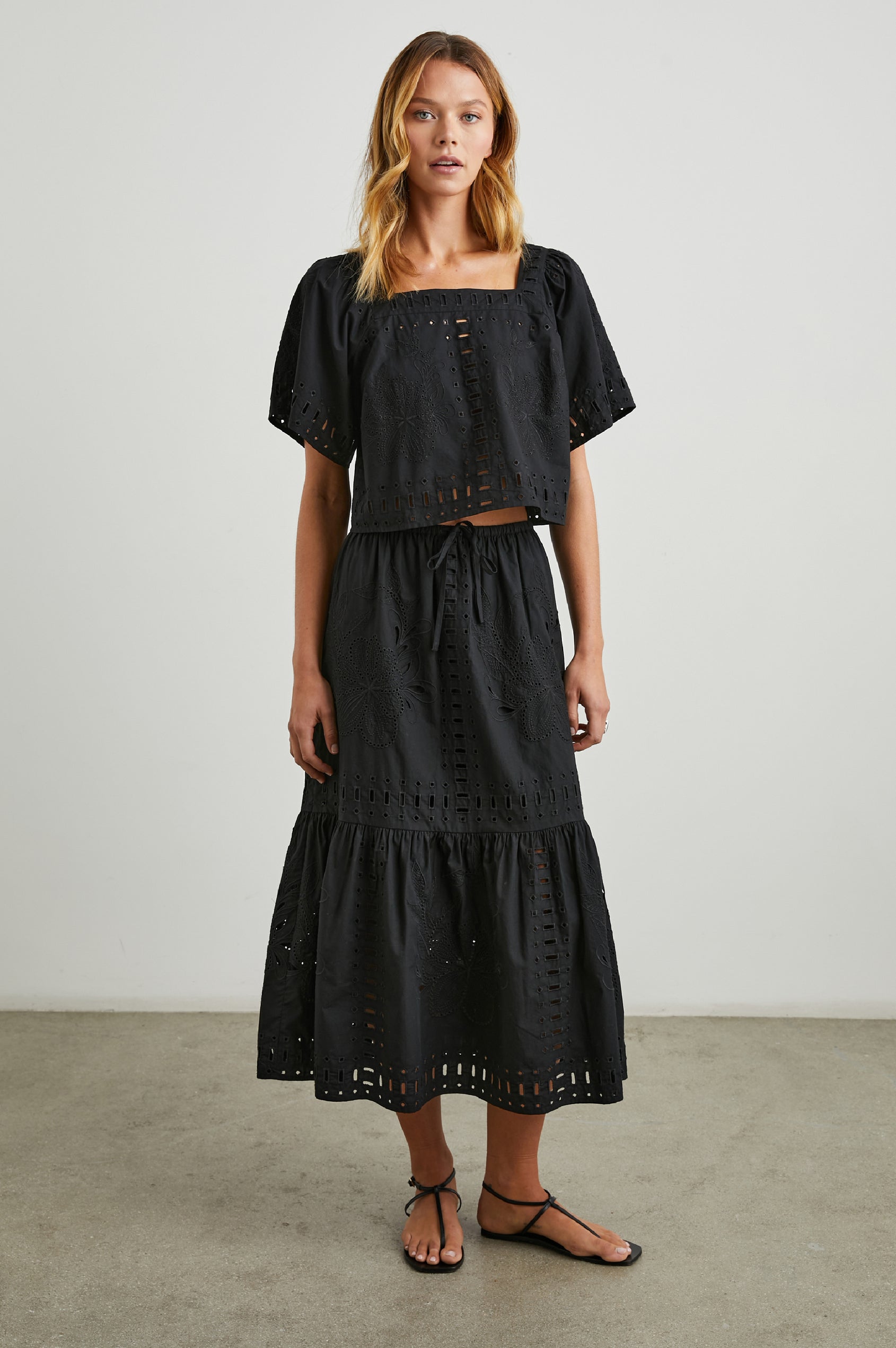 Laine Short Sleeve Crop Top with Square Neckline, and a Floral and Geometric Eyelet Design in Black Colorway - Front Full Body View Featured on Model