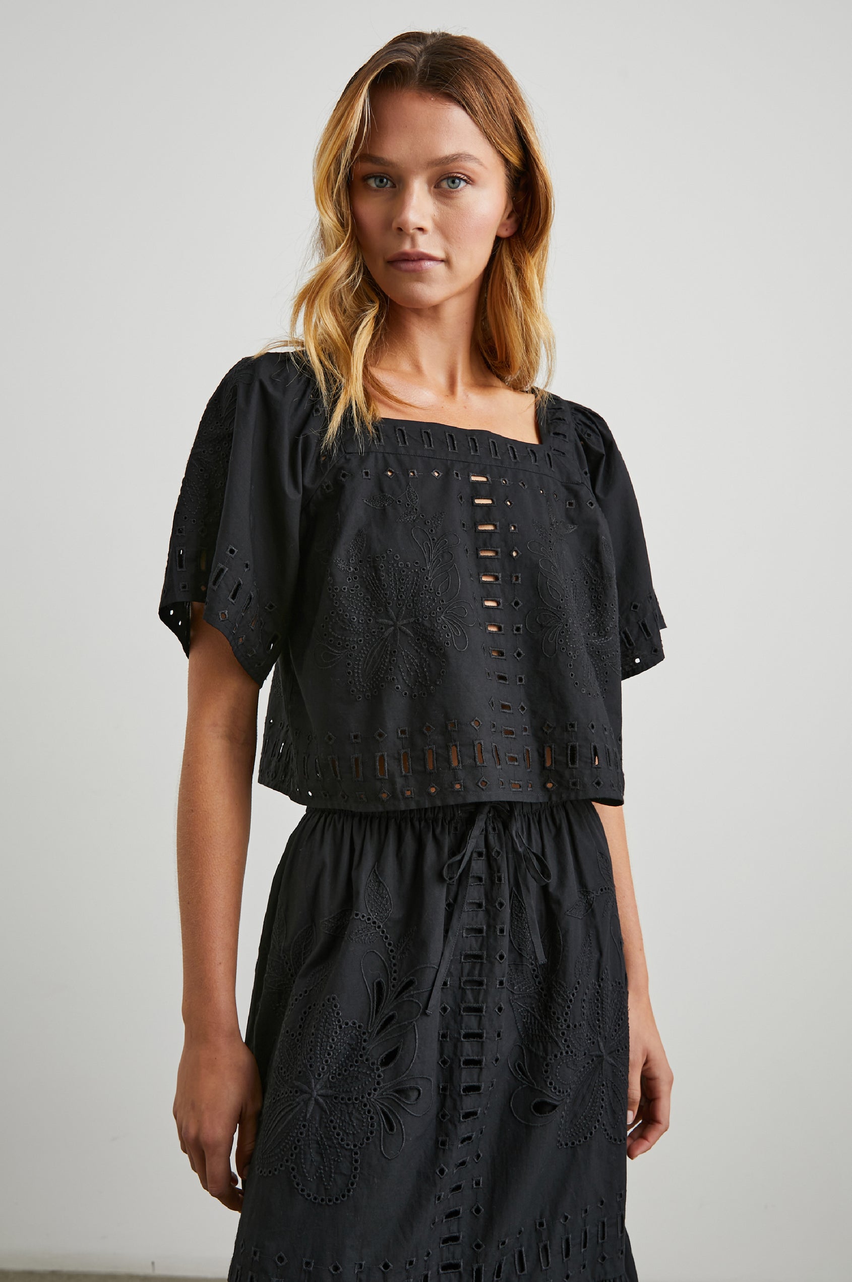 Laine Short Sleeve Crop Top with Square Neckline, and a Floral and Geometric Eyelet Design in Black Colorway - Front View Featured on Model