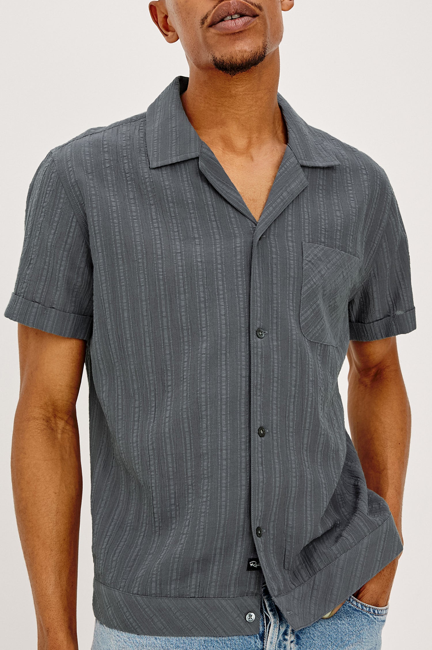 Lemmy is a textured dobby cotton shirt. Featuring a notched collar, chest pocket, front buttons, and rolled short sleeves - close up front upper body view on model.