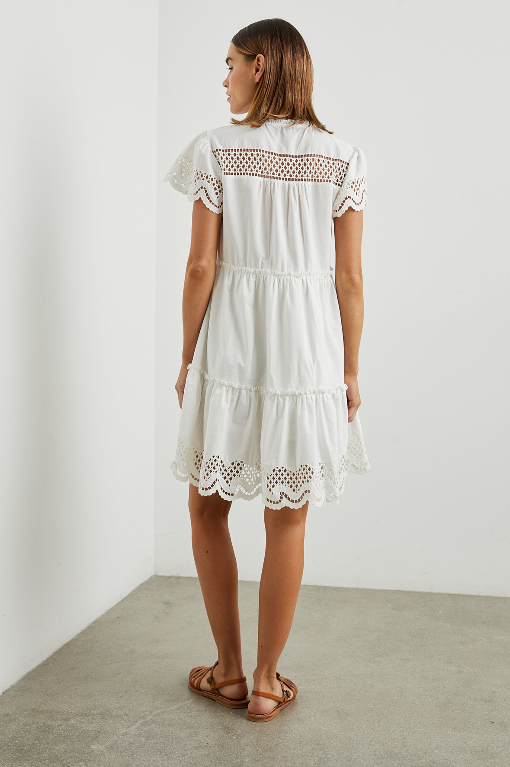 Lettie Short Sleeve Mini Dress with a Button Keyhole Neckline, a Tiered Skirt, and an Eyelet Design on the Yoke, Sleeves and Hem in White Colorway - Back Full Body View Featured on Model 