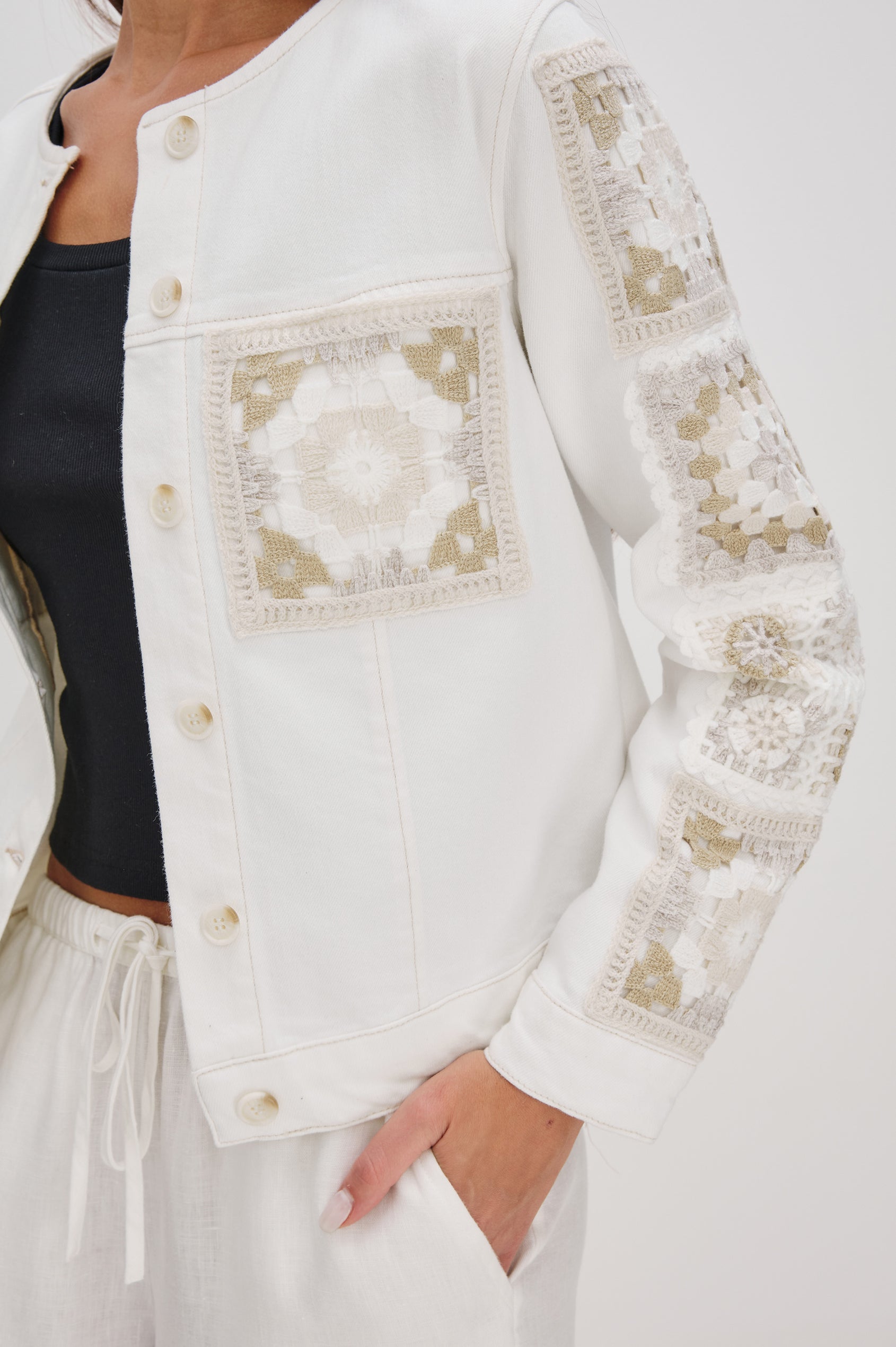 Lido collarless denim jacket with contrast embroidery details, chest pockets and embellishment buttons in vintage ecru crochet colorway. Front detail view on model.